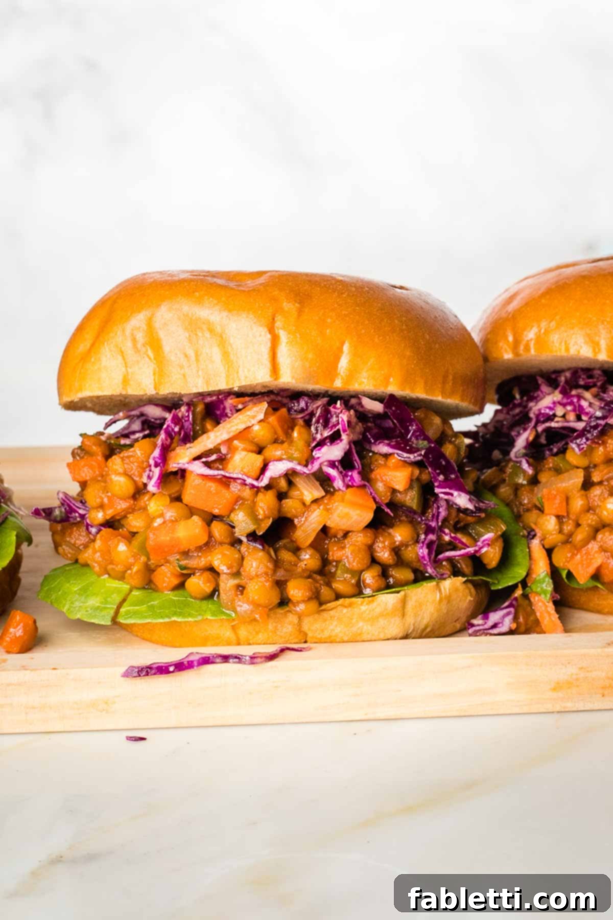 Head on shot of a vegan sloppy joe sandwich with tomato sauce, purple cabbage and a piece of green lettuce.