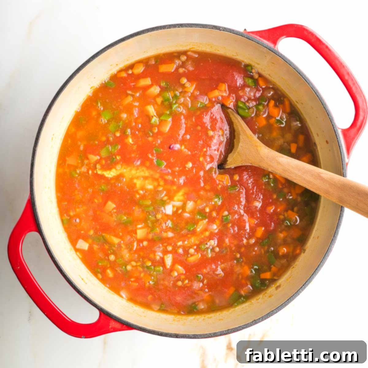 Veggies and lentils in a red tomato sauce, stirred with wooden spoon.
