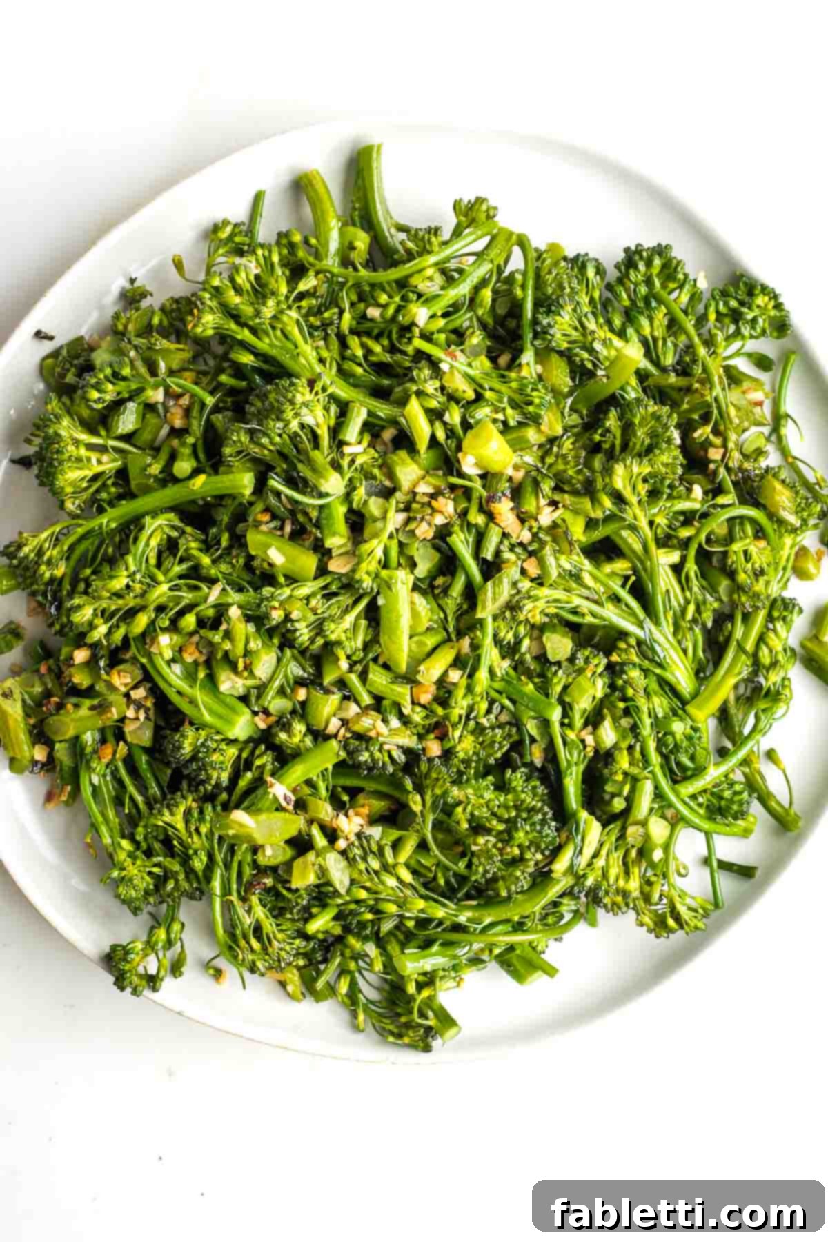 Sauteed baby broccoli and garlic with crushed red pepper on a white platter.