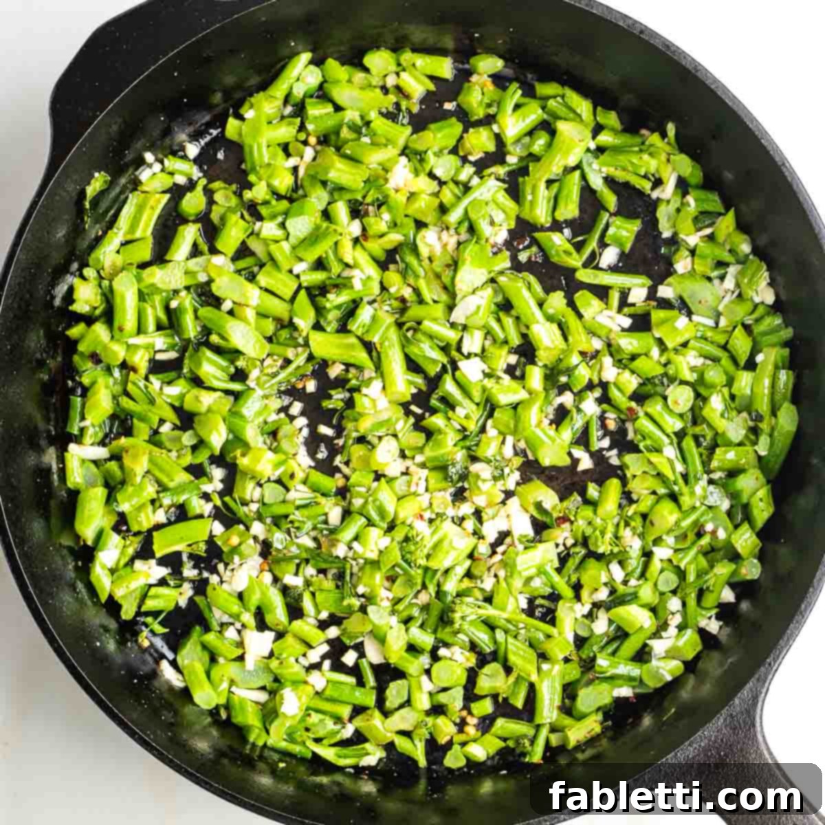Chopped baby broccoli stems in a cast iron skillet with minced garlic.