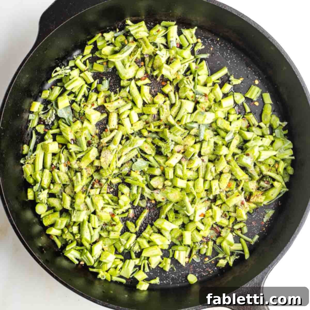 Sliced broccolini stems in a cast iron skillet with crushed red pepper and salt.