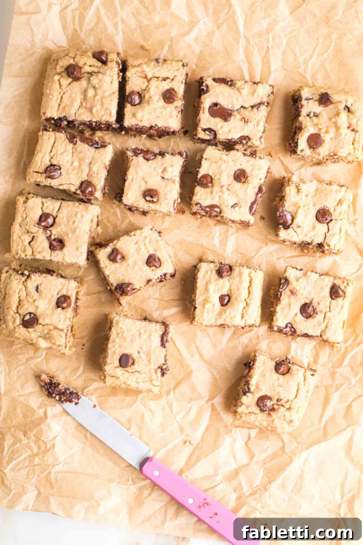 Bean-Powered Vegan Blondies 2 White bean blondies with chocolate chips, cut into squares with a pink knife.