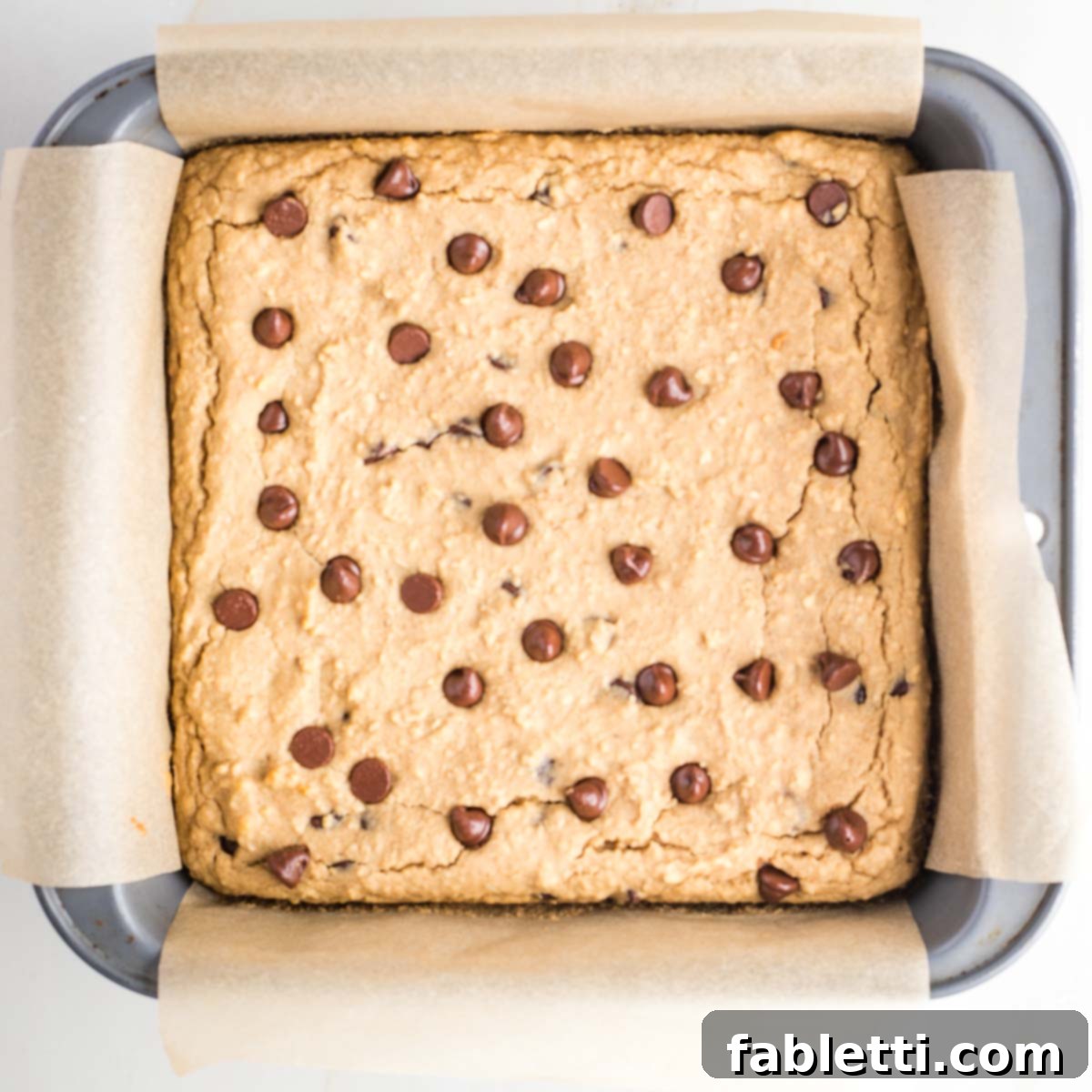 Bean-Powered Vegan Blondies 12 Baked blondies with chocolate chips in a square baking pan with parchment paper.