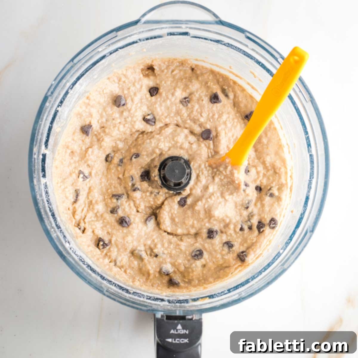 Bean-Powered Vegan Blondies 10 Spatula mixing chocolate chips into blondie batter in the bowl of a food processor.