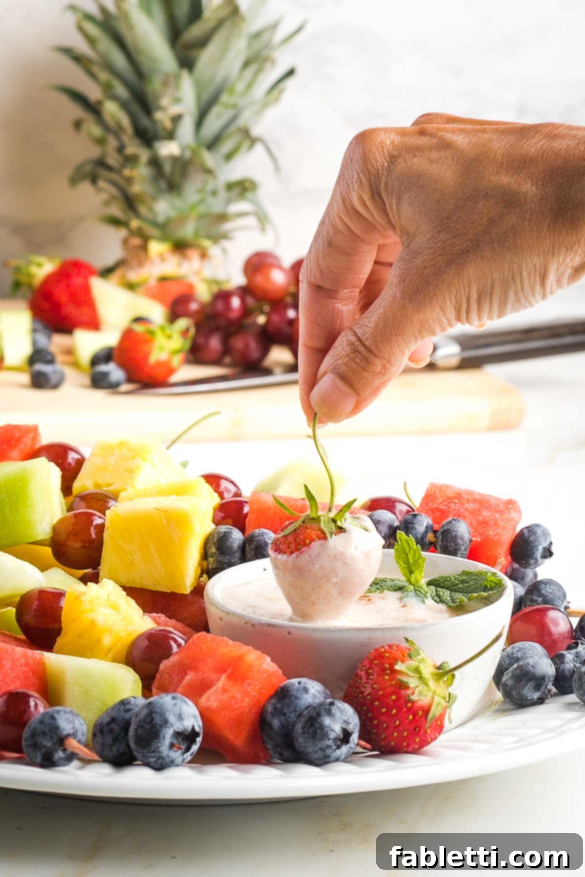 Velvety Vegan Fruit Dip 2 Strawberry coming out of fruit dip, on a platter of colorful assorted fruit skewers.