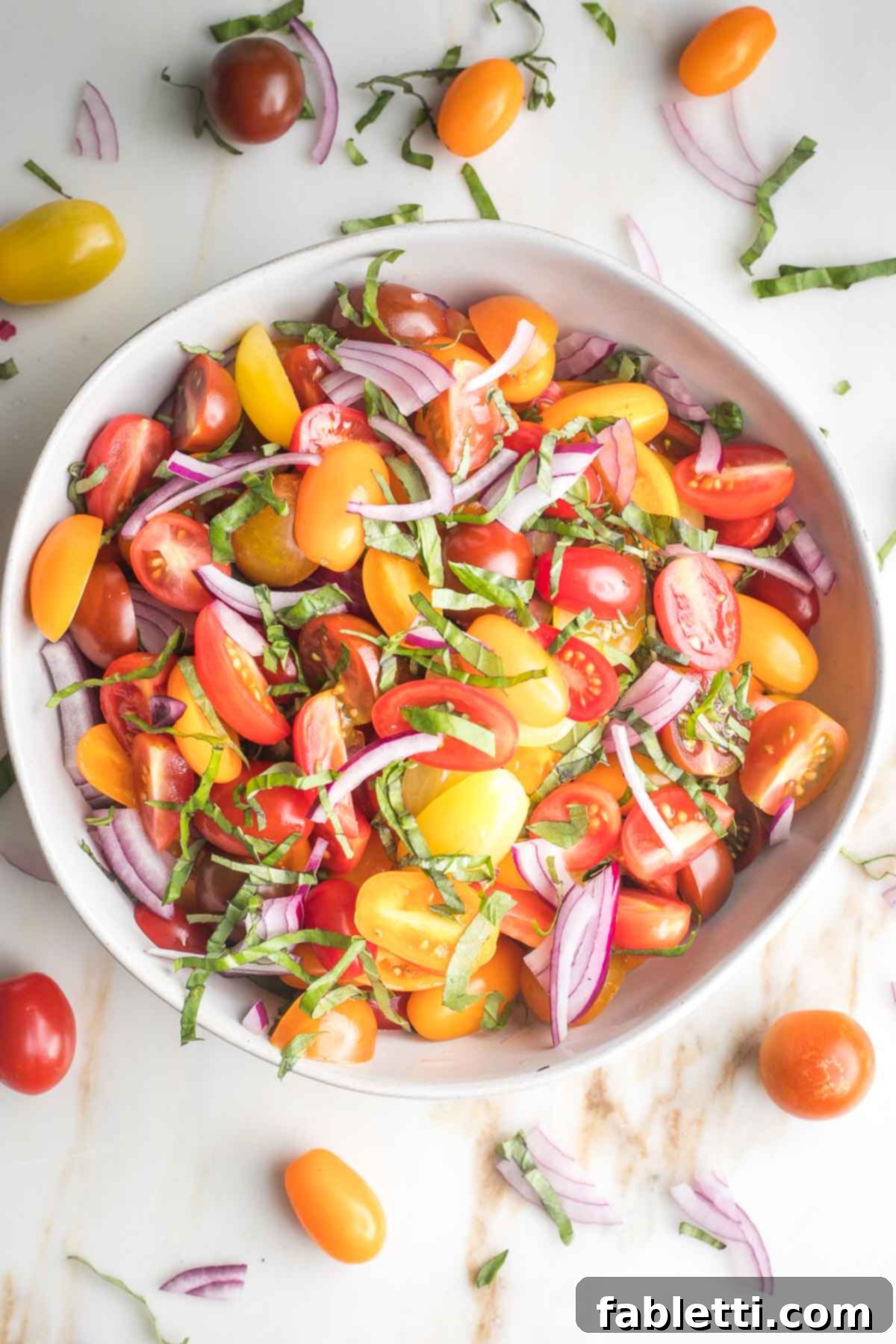 Sun-Kissed Tomato and Onion Salad with Balsamic Drizzle 6 Vibrant yellow, orange and red tomatoes with onion slices and fresh basil in a white bowl.