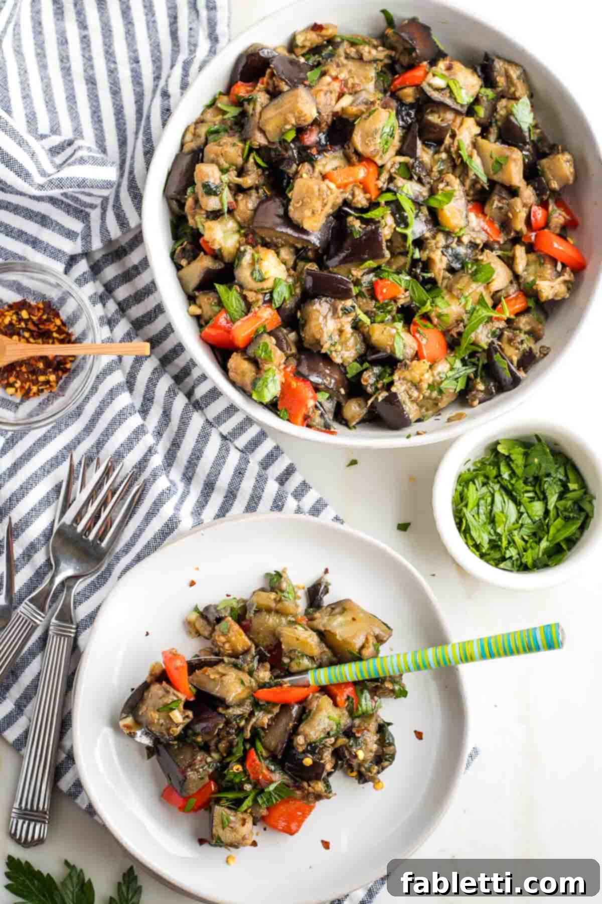 Savory Sautéed Eggplant Salad 2 A large bowl of colorful sauteed eggplant salad featuring tender eggplant cubes, bright red peppers, and fresh green parsley. A smaller plate with a portion of the same salad sits beside it, ready to be enjoyed.