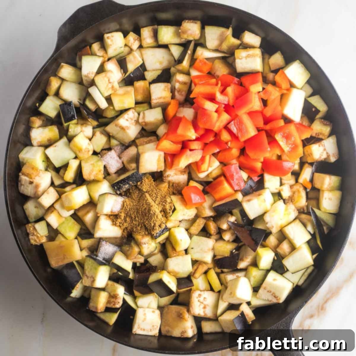 Savory Sautéed Eggplant Salad 11 Cubes of eggplant with diced red peppers and a generous heap of cumin added to a cast iron skillet, mid-sauté.