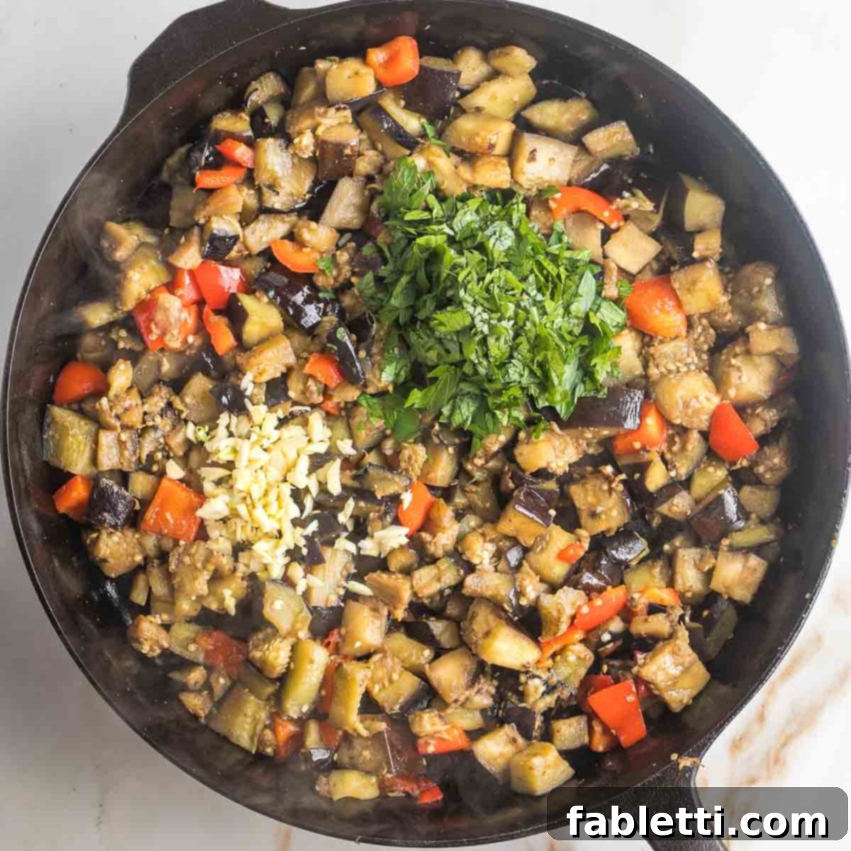 Savory Sautéed Eggplant Salad 12 Sauteed eggplant and red peppers in a cast iron skillet, topped with a pile of chopped parsley and minced garlic, before final stirring.