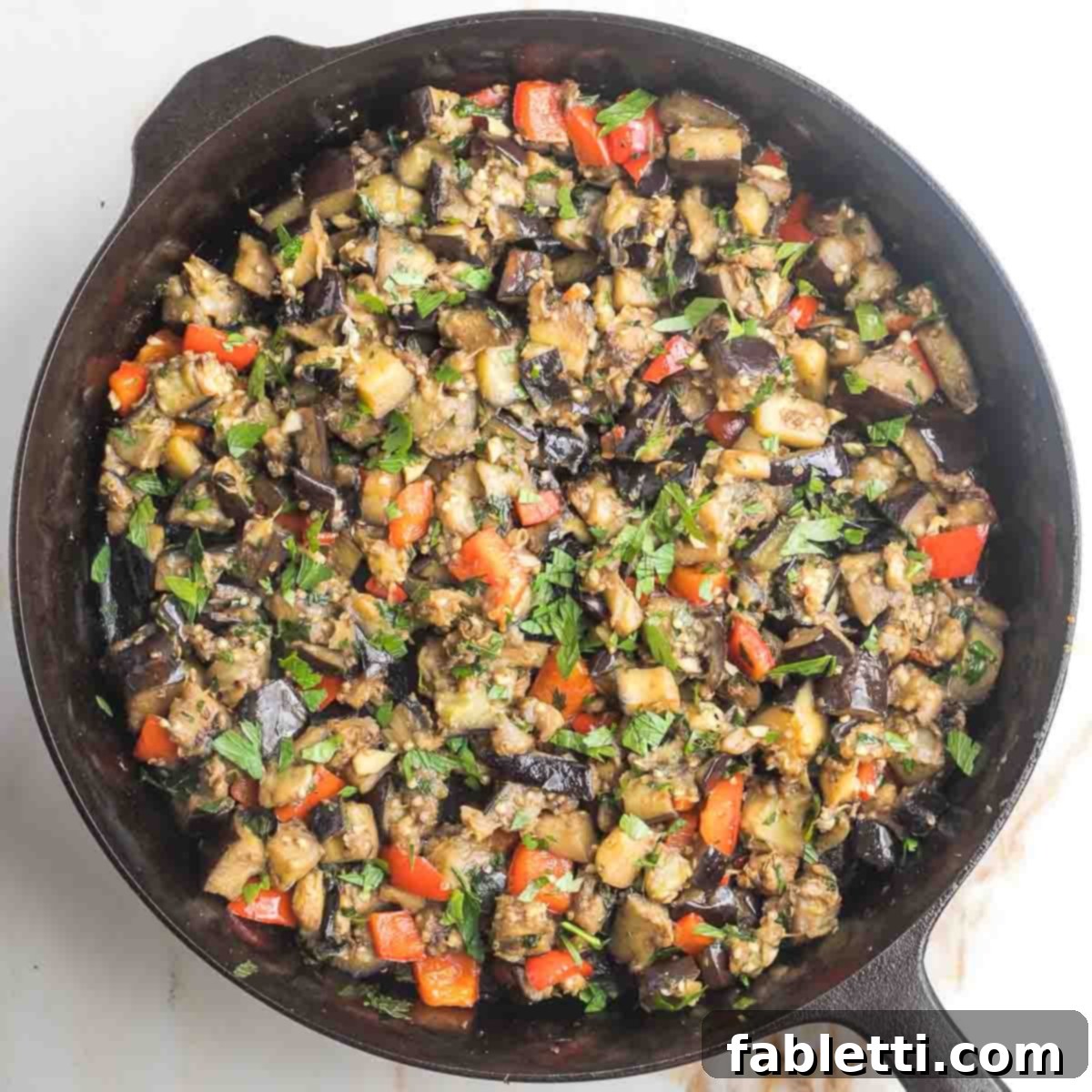 Savory Sautéed Eggplant Salad 13 The finished sauteed eggplant salad, with tender eggplant cubes, red bell pepper, fresh parsley, garlic, and spices, mixed thoroughly in a cast iron skillet.