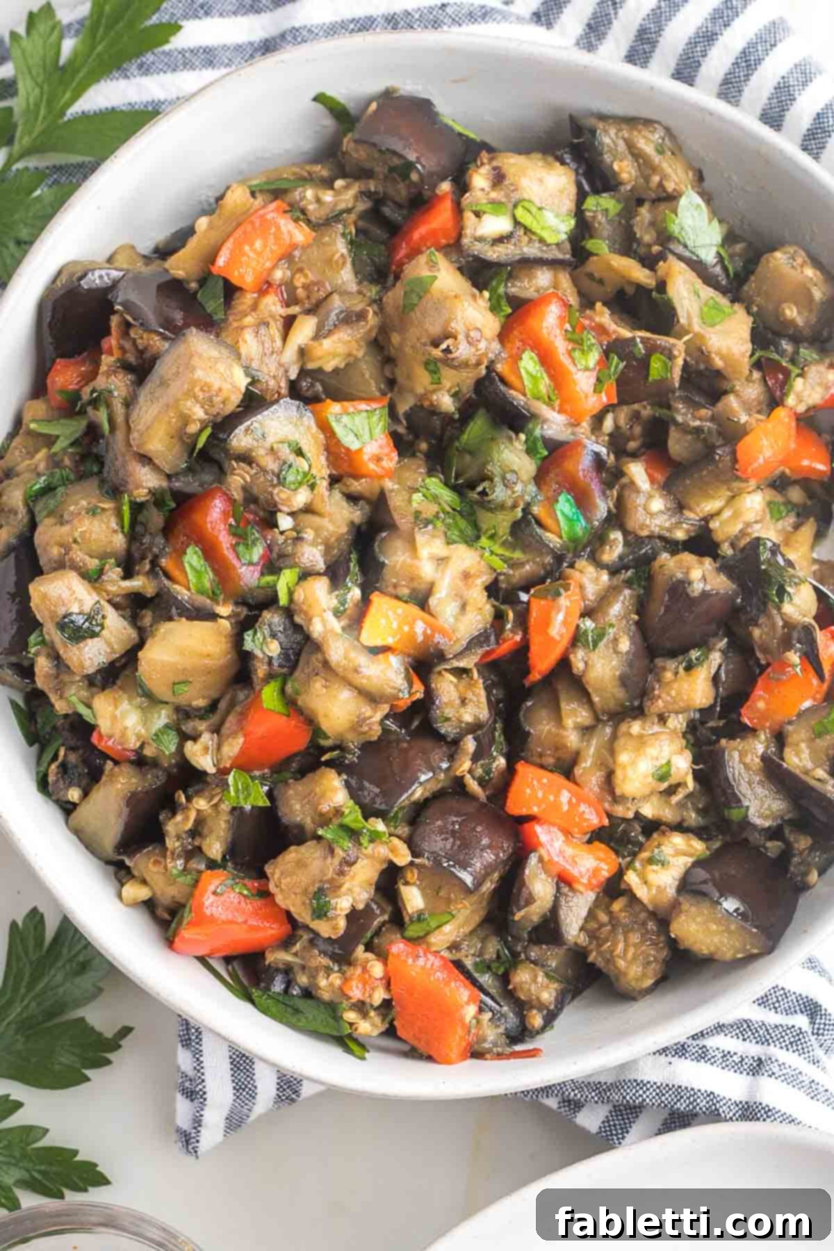 Savory Sautéed Eggplant Salad 14 A beautiful bowl of eggplant salad, showcasing sauteed eggplant cubes perfectly mixed with red pepper, garlic, and vibrant fresh parsley, ready to be served.