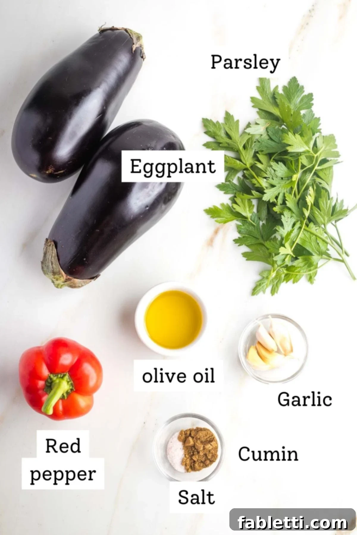 Savory Sautéed Eggplant Salad 3 Fresh ingredients laid out for sauteed eggplant salad, including whole eggplants, red bell pepper, garlic cloves, and a bunch of fresh parsley.