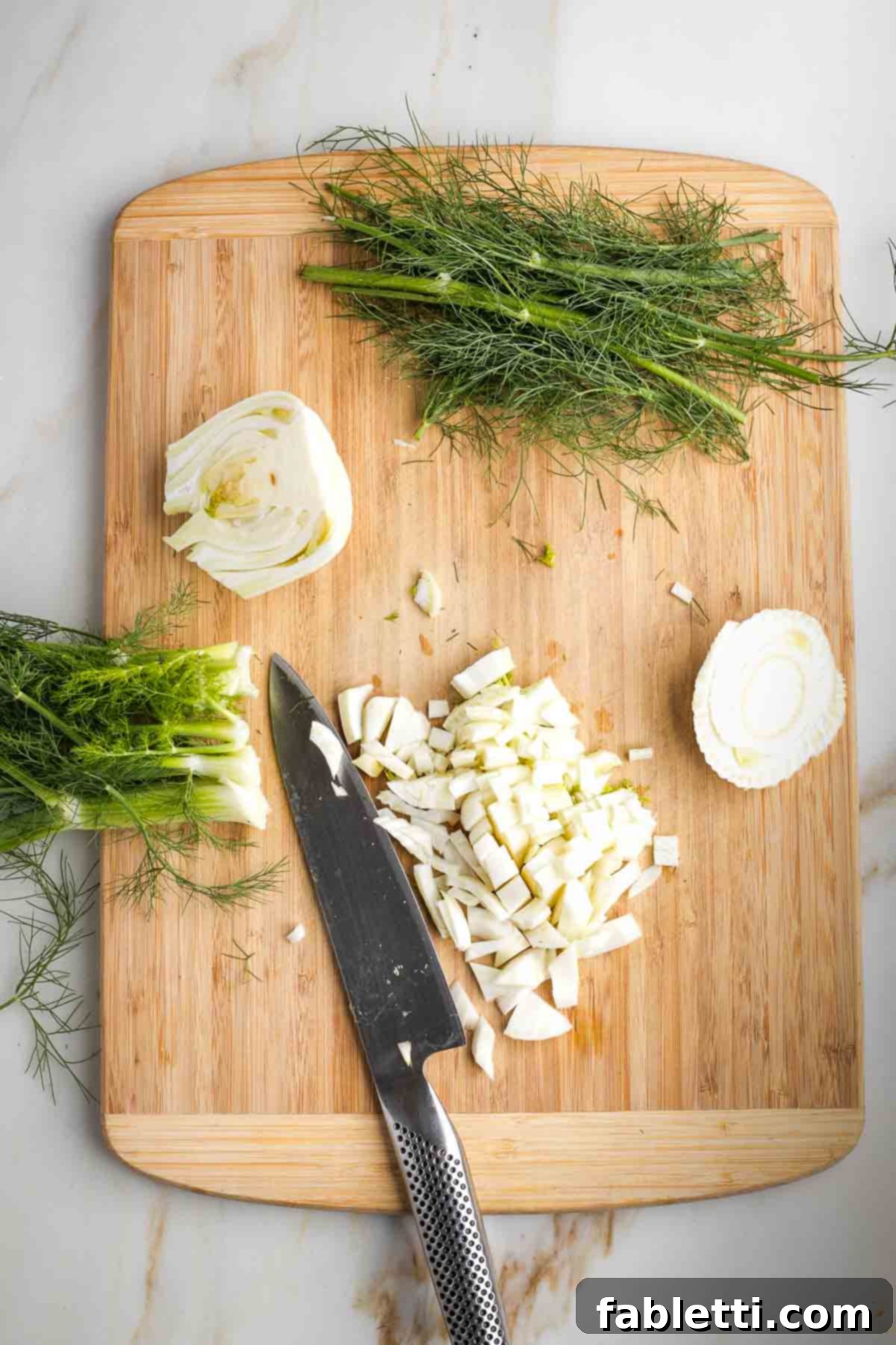 Fennel bulb being diced on a cutting board, with its woody bottom and fronds already removed.