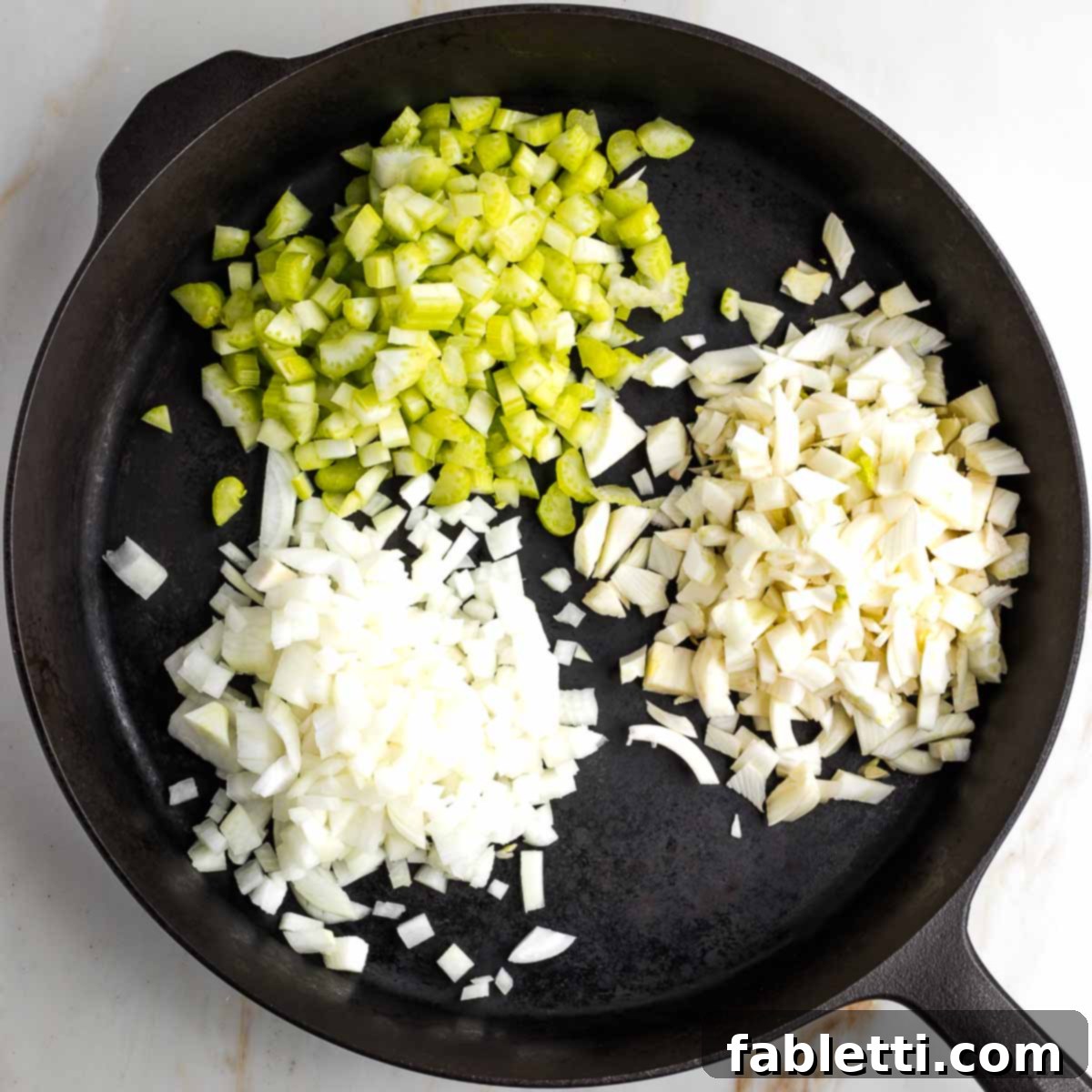 A cast iron skillet containing chopped onion, fennel, and celery, beginning to soften and caramelize.