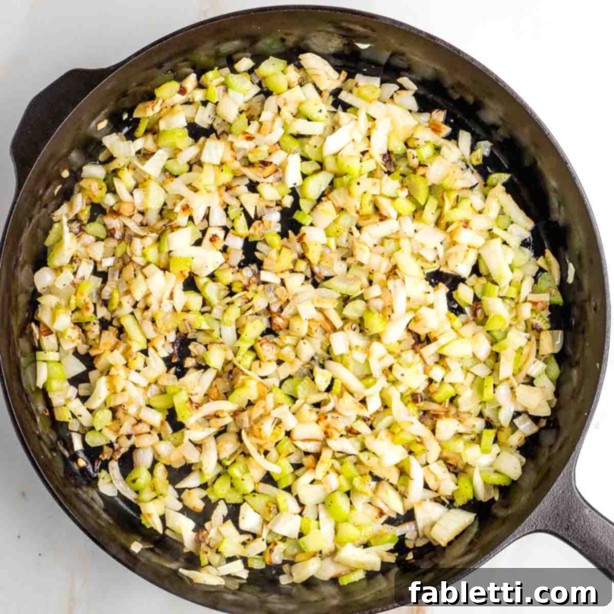 Sautéed celery, onion, and fennel in a cast iron skillet, now golden brown and caramelized.