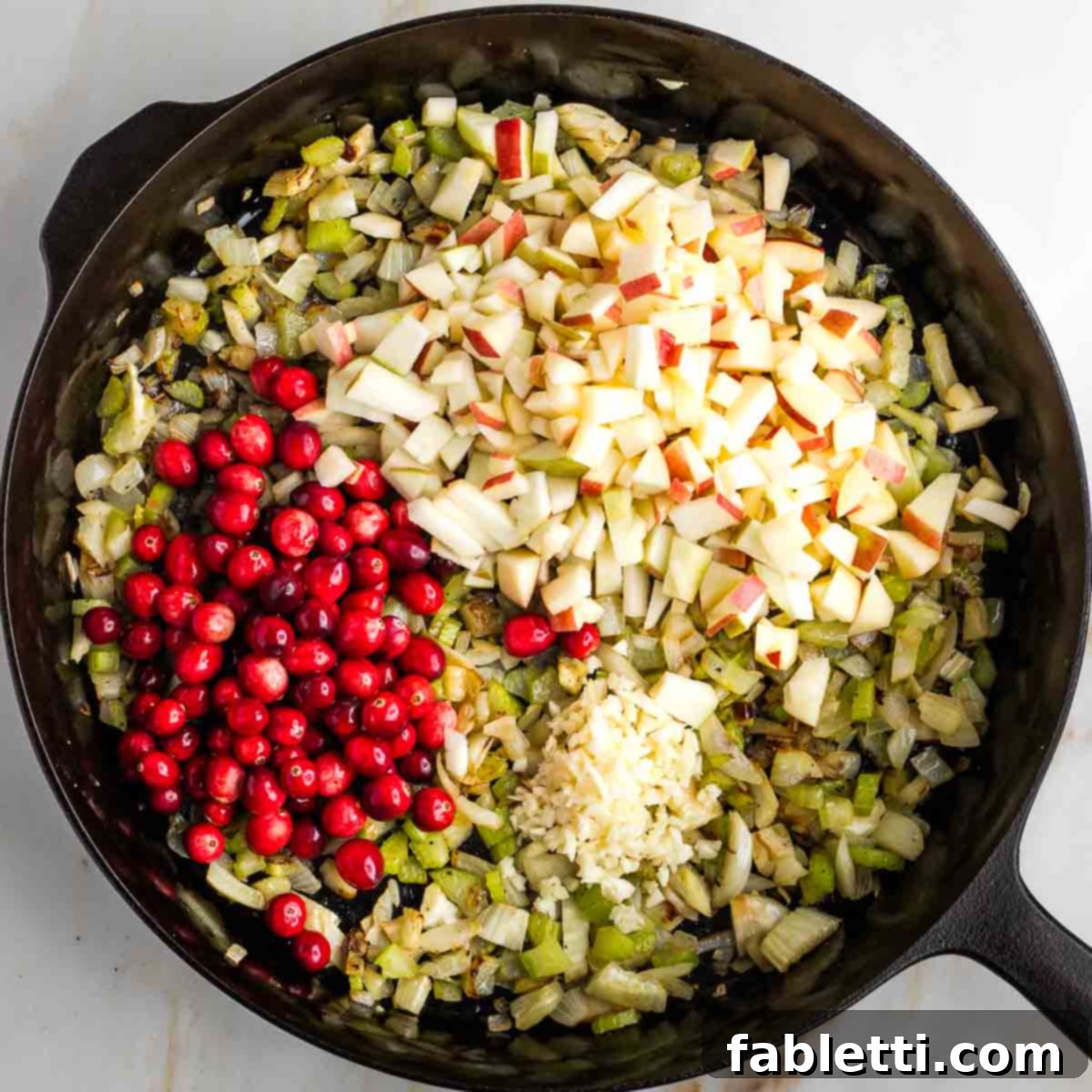 Sauteed vegetables with fresh cranberries, chopped apples, and minced garlic added on top, ready to be cooked further.