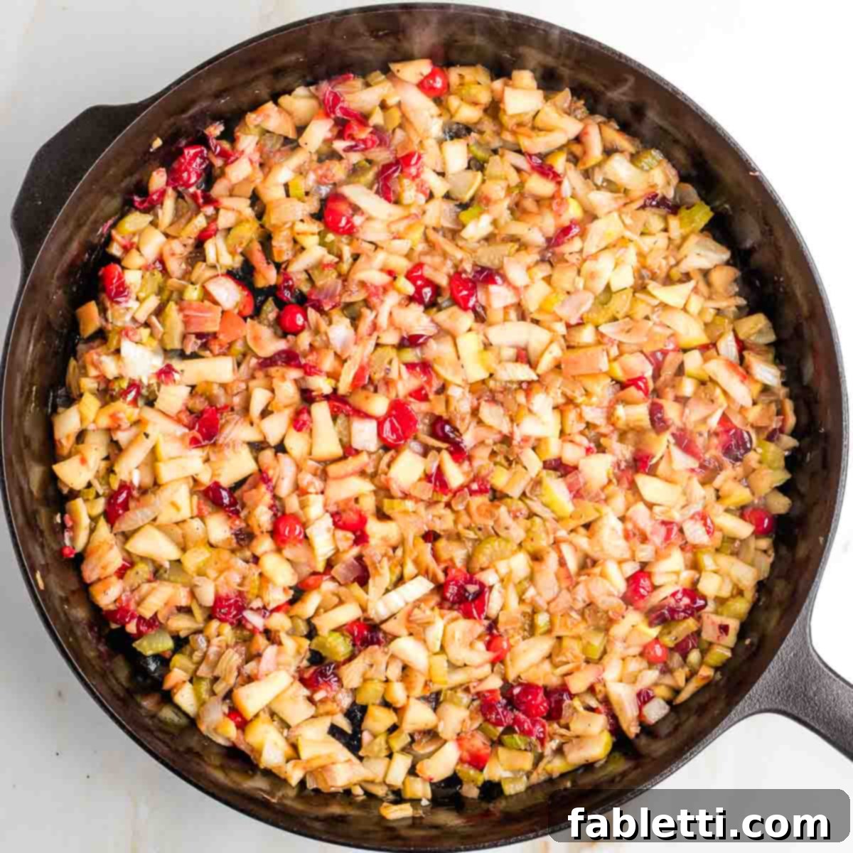 Skillet with sautéed vegetables, cranberries, and apples, cooked until the cranberries have softened and burst.