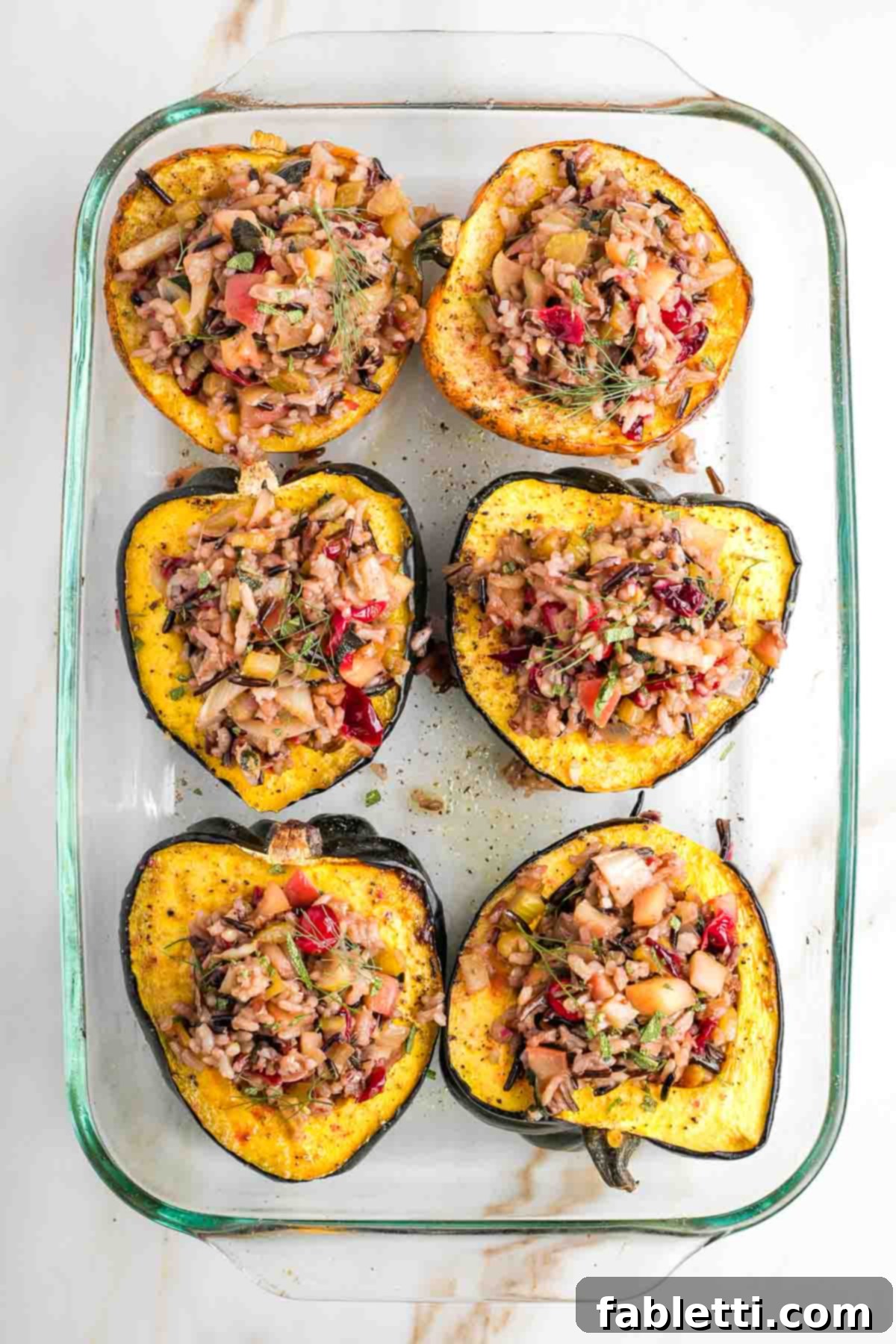 Halved acorn squash generously filled with the vibrant vegan wild rice stuffing, ready for a final bake.