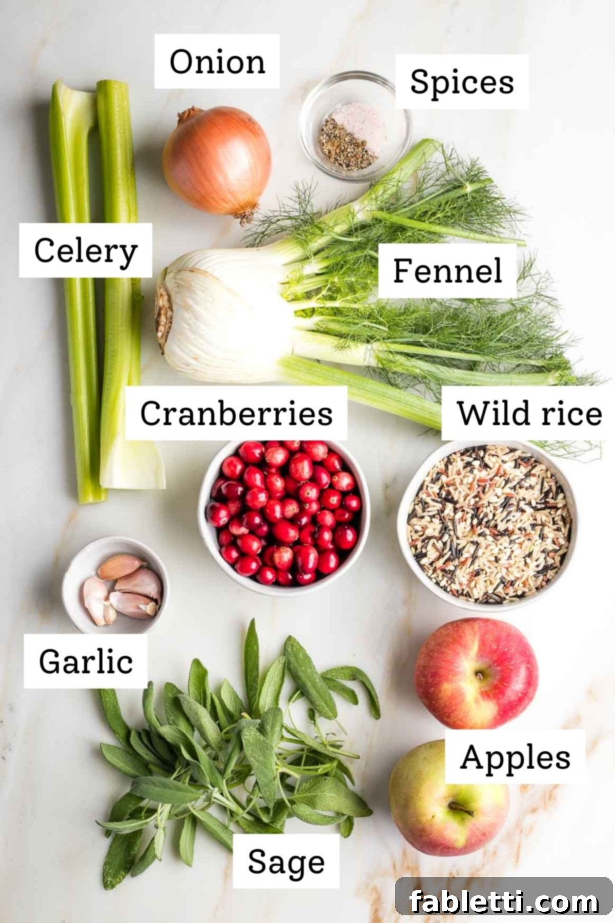 A vibrant display of fresh ingredients for the stuffing, including wild rice, onions, celery, fennel, apples, cranberries, garlic, and sage, artfully arranged on a wooden surface.
