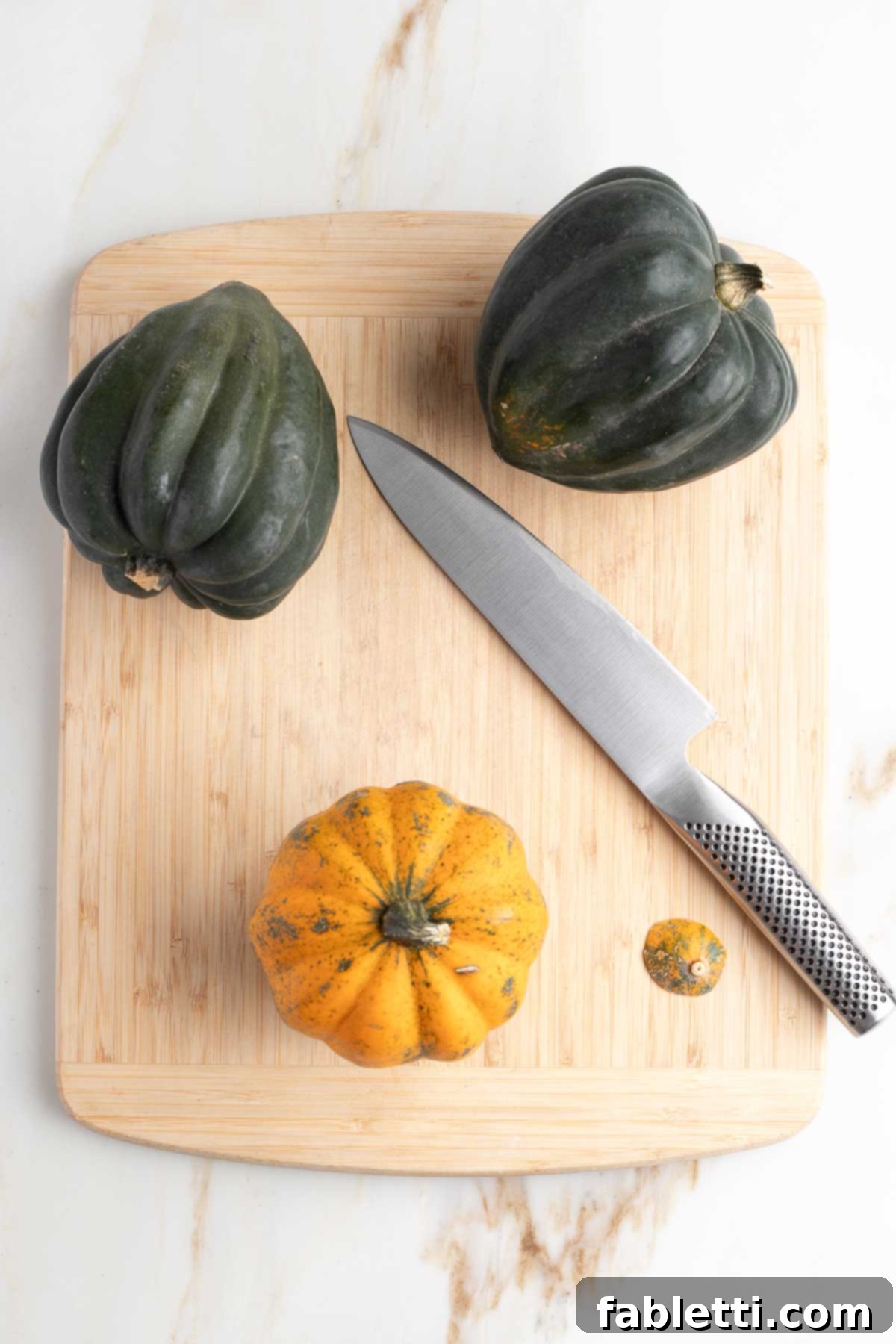 Three acorn squash on a cutting board, with one standing upright after a small sliver has been cut off its bottom to create a stable base.