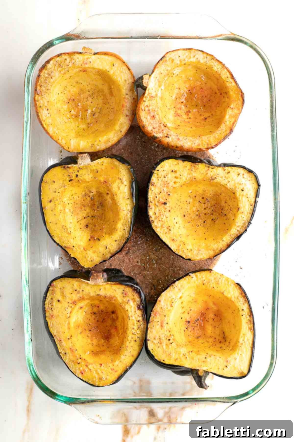 Roasted acorn squash halves in a baking dish, cooked until golden and tender.