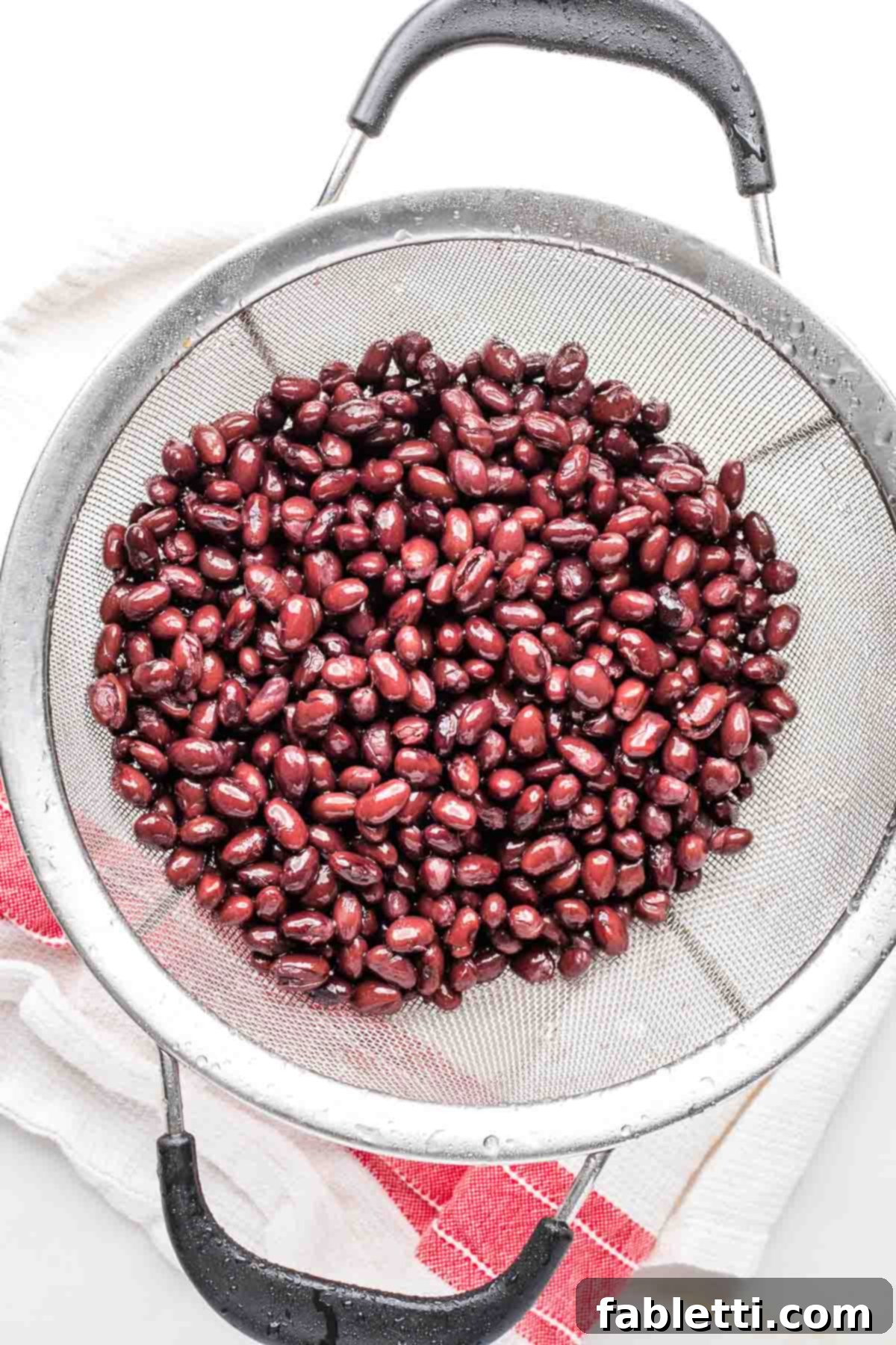 Crunchy Taco Black Beans 4 Mesh sieve filled with black beans and droplets of water. The beans are fresh out of the can and being rinsed.