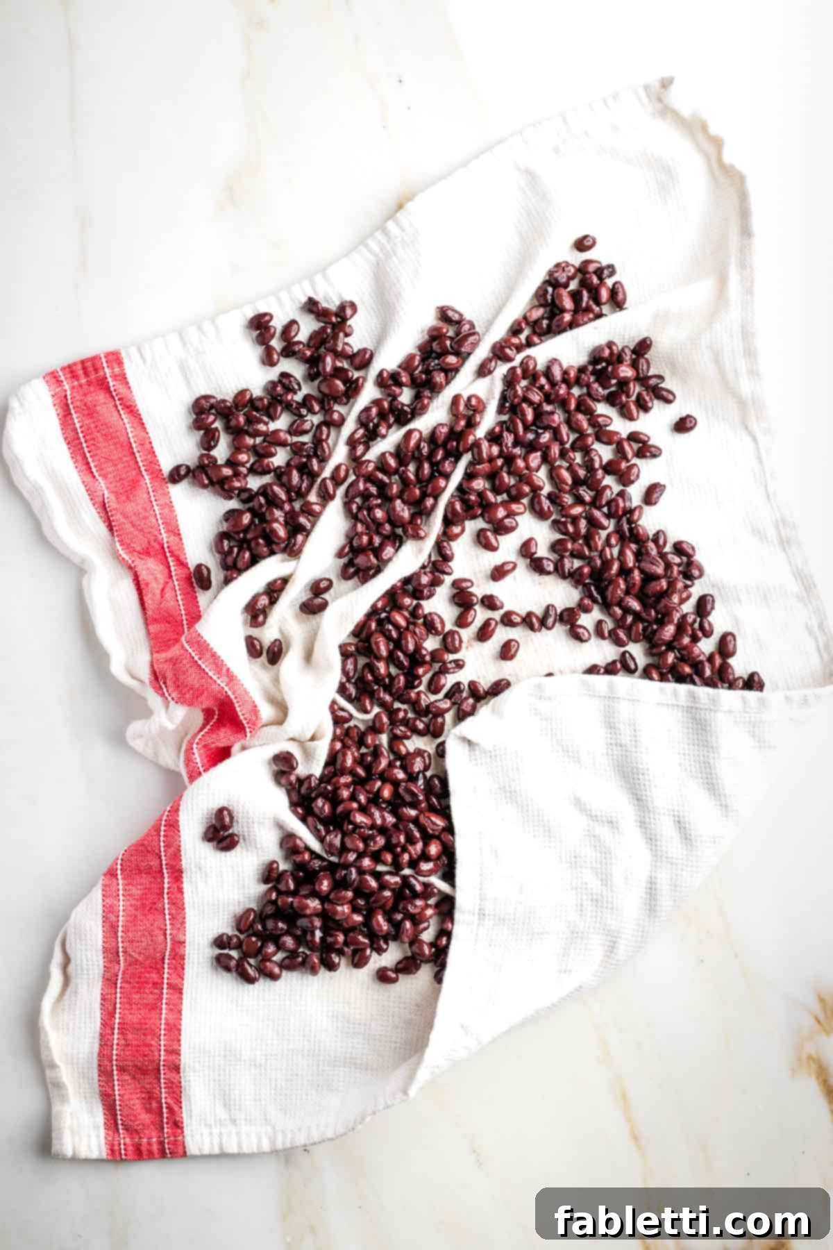 Crunchy Taco Black Beans 5 Black beans spread on a white kitchen towel with red trim, being patted dry. This illustrates the importance of removing moisture.