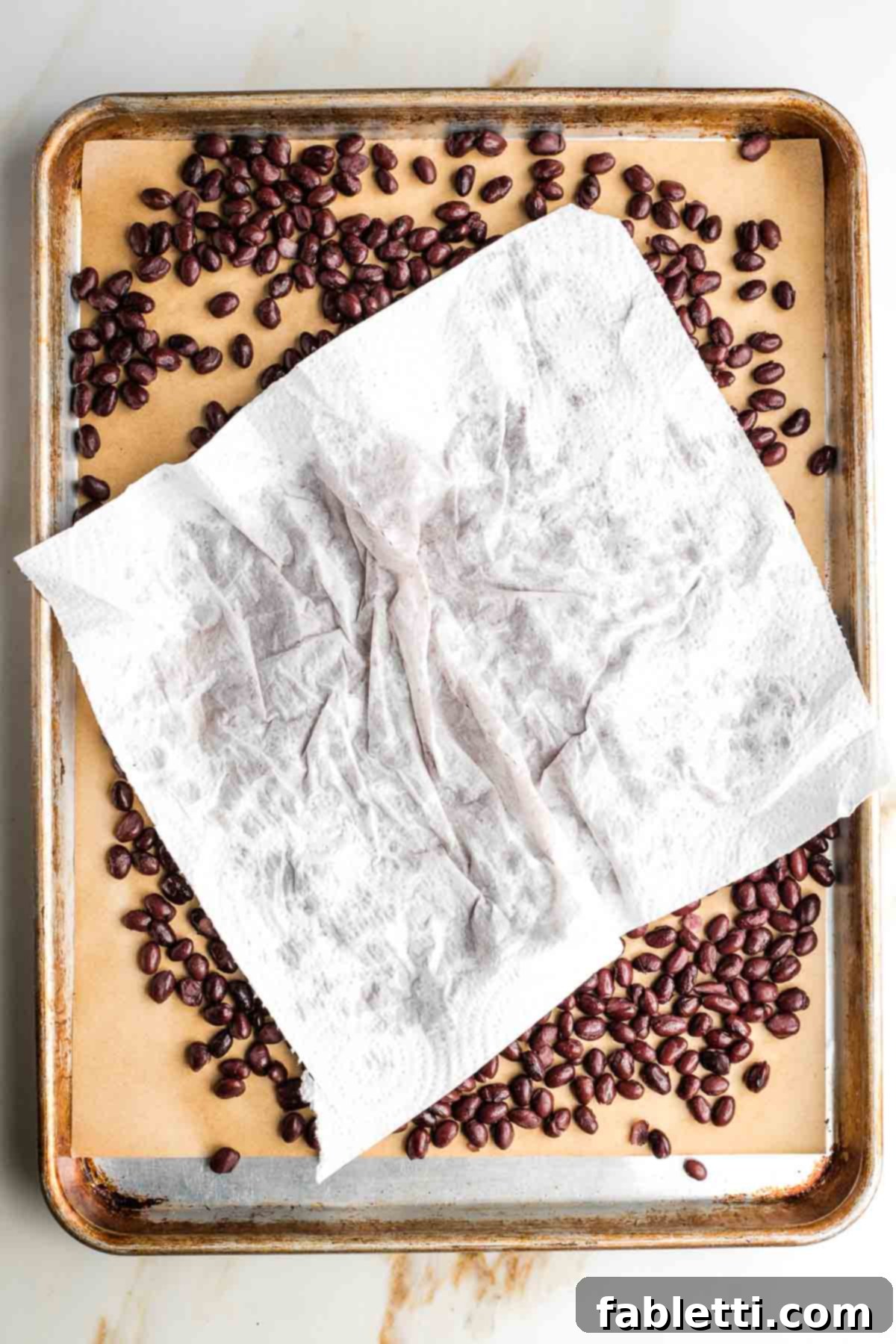 Crunchy Taco Black Beans 6 Sheet pan lined with parchment, filled with black beans and a paper towel, blotting them dry. A final check for moisture.