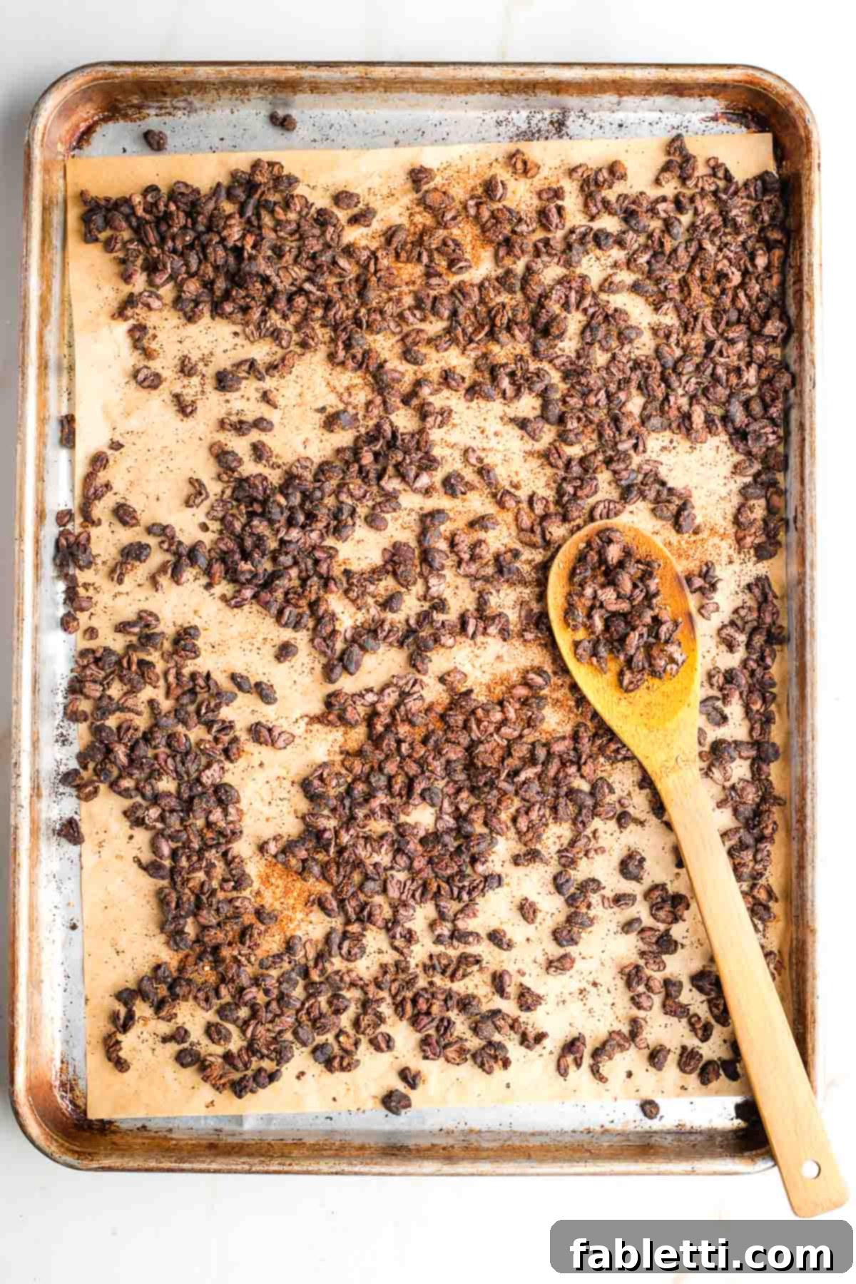 Crunchy Taco Black Beans 8 Baking tray with roasted black beans, some on a wooden spoon. Mid-roasting stage.