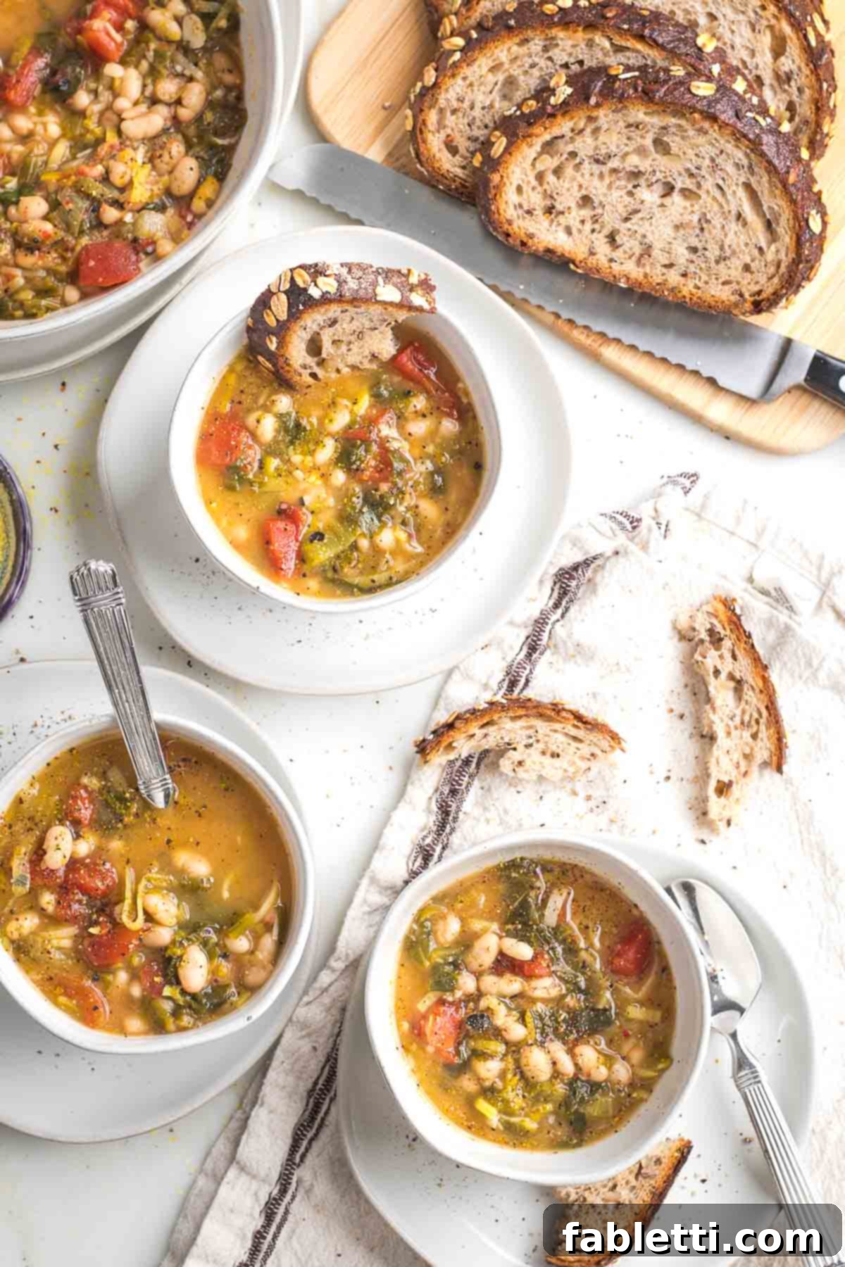 Bowls of chunky soup with wilted greens, tomatoes, and white beans. Also some sliced sourdough with pieces dipped into the bowls of soup.