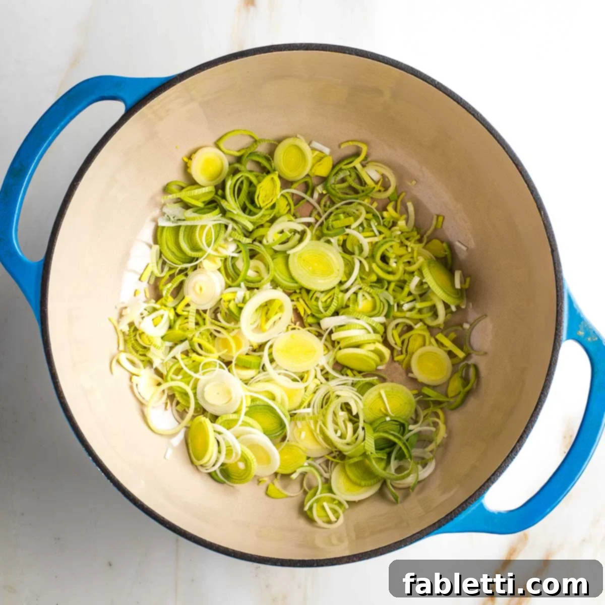 Light blue dutch oven with sliced leeks in the bottom.