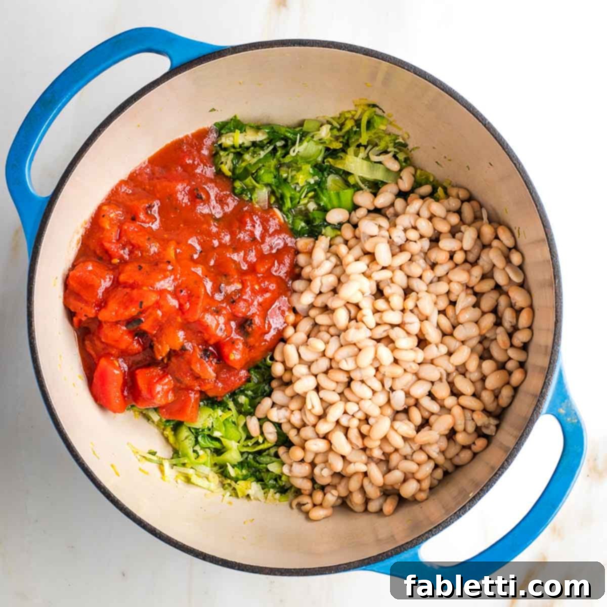 Bottom of dutch oven filled with wilted greens and then diced tomatoes and white beans.