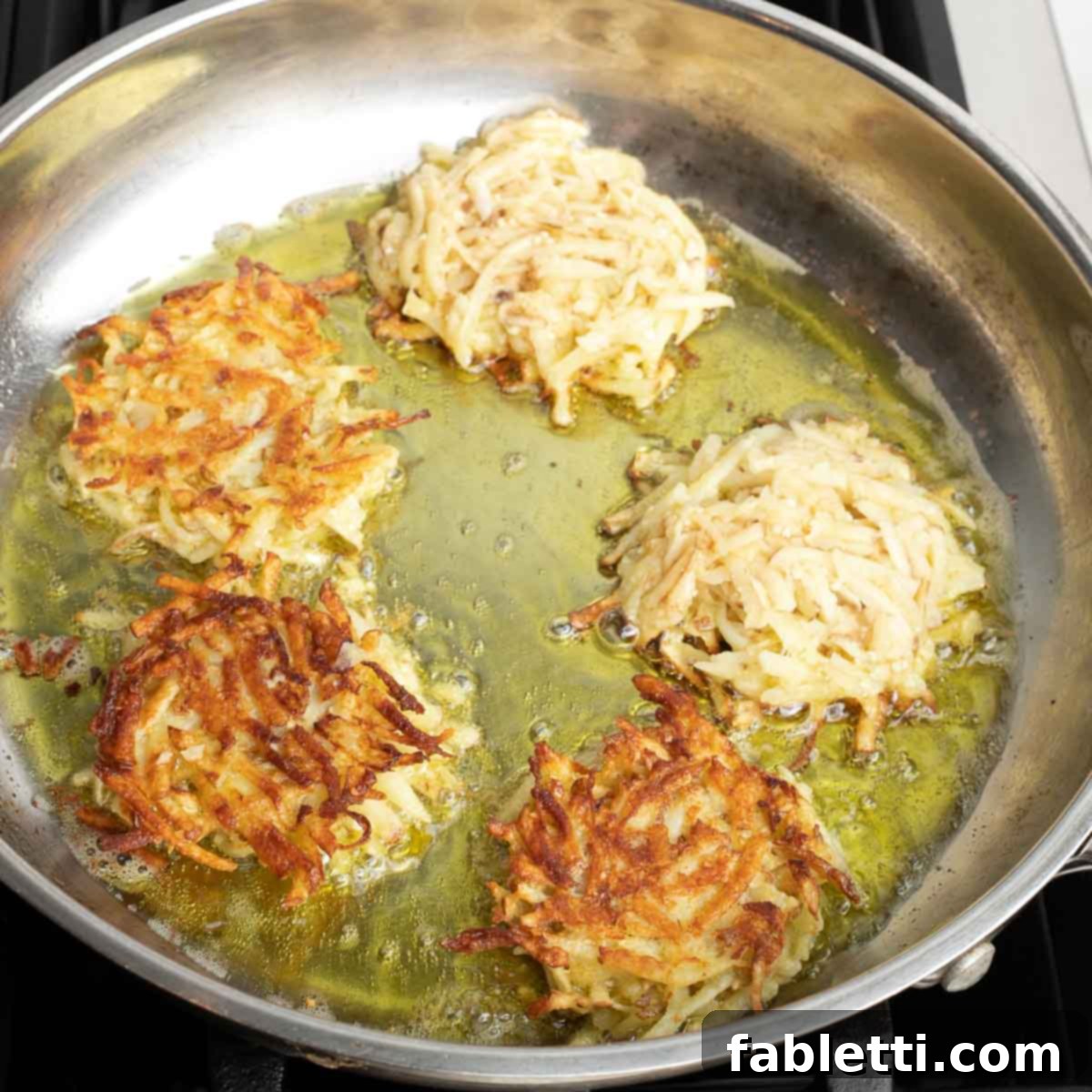 Grandma's Golden Potato Latkes 11 Multiple potato latkes frying in a large skillet with hot oil, some already flipped to reveal their golden-brown undersides.