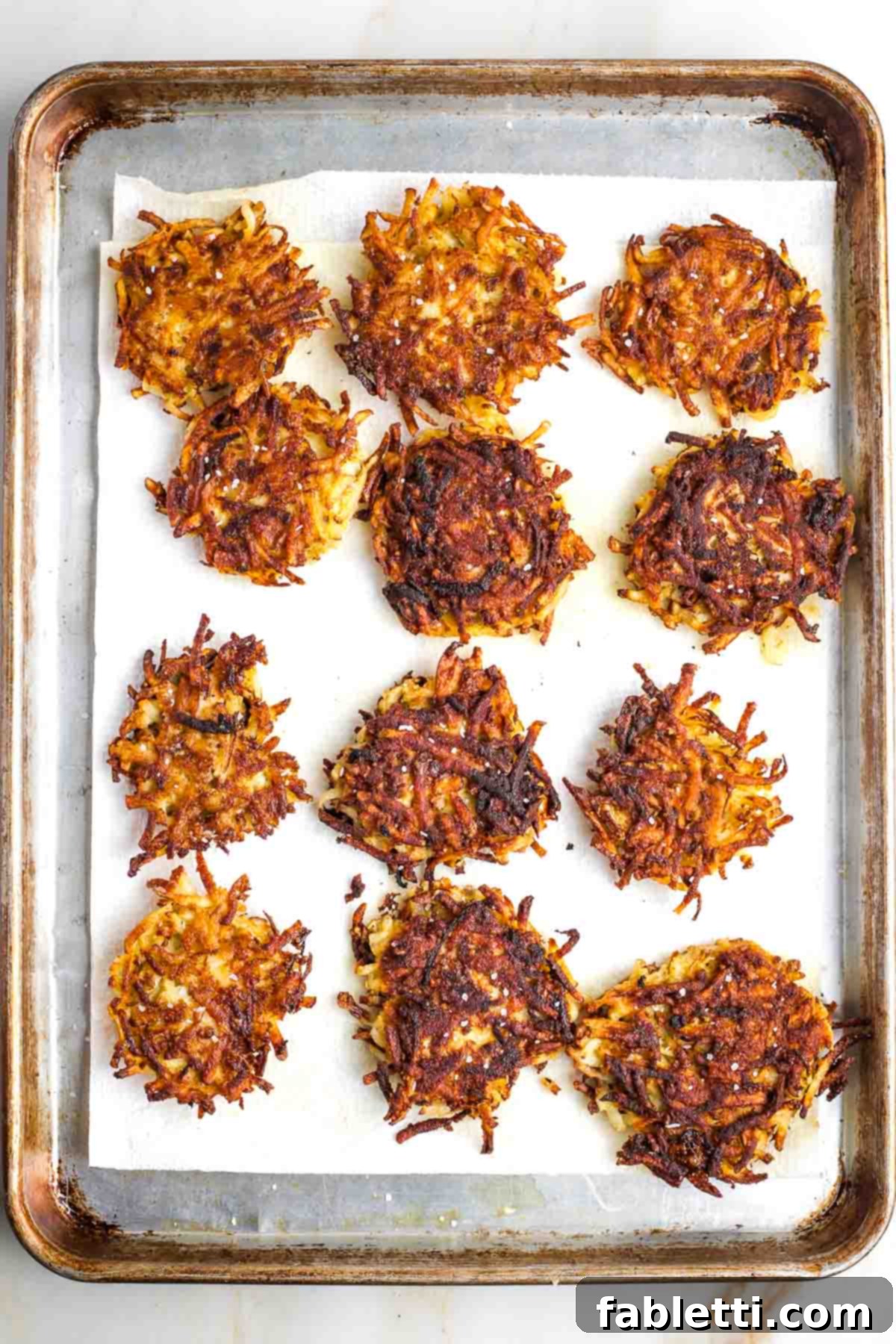 Grandma's Golden Potato Latkes 12 Freshly fried potato latkes cooling on paper towels to drain excess oil, sprinkled with salt.