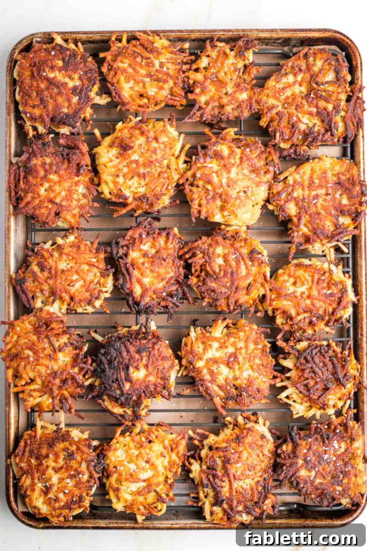 Grandma's Golden Potato Latkes 13 A baking sheet with a wire rack, holding several freshly fried potato latkes, ready to be kept warm in the oven.