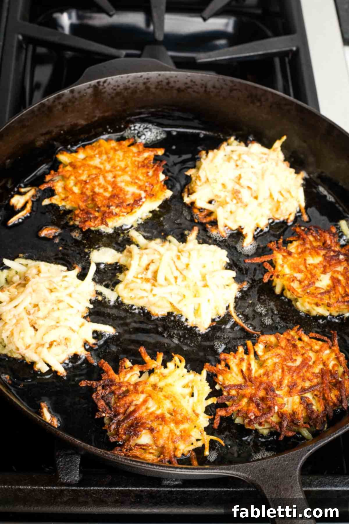 Grandma's Golden Potato Latkes 14 A cast iron skillet filled with hot oil and frying potato latkes, some already turned to reveal their perfectly crispy edges.