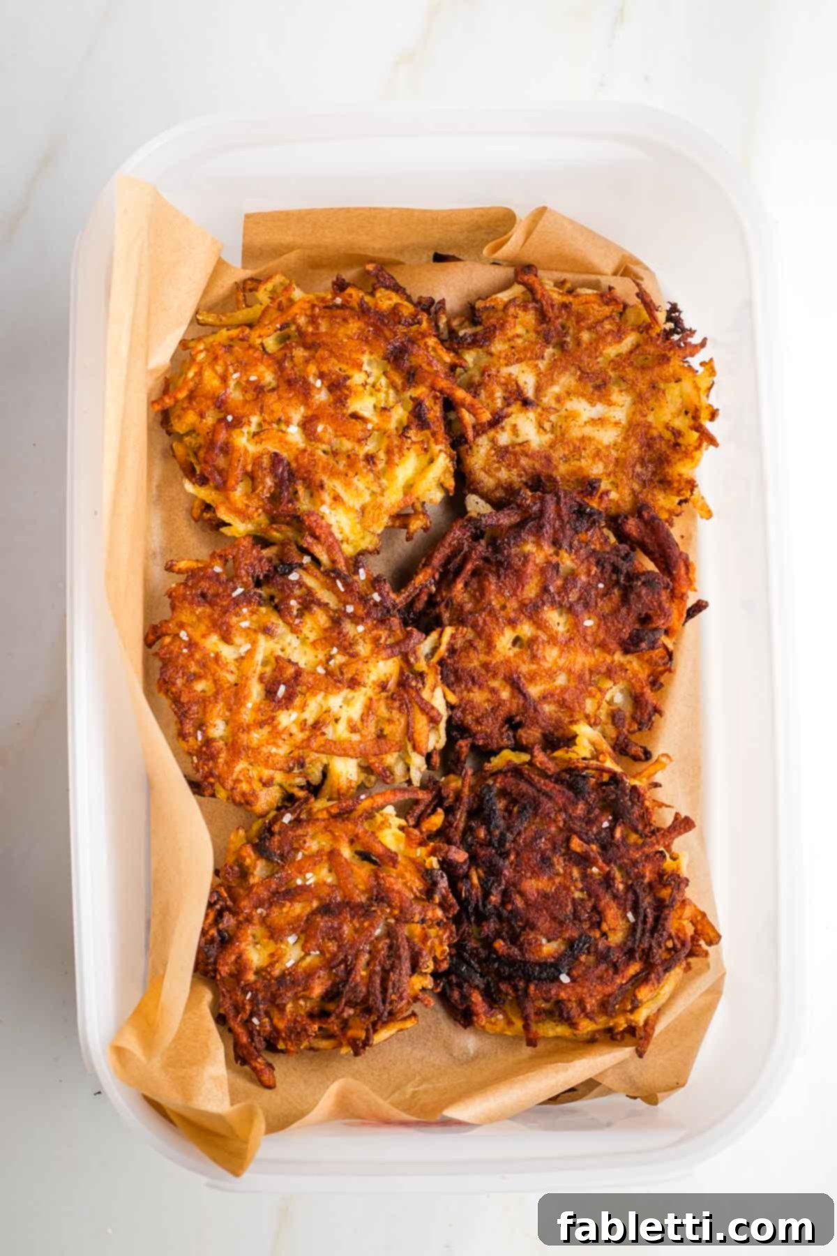 Grandma's Golden Potato Latkes 17 A large airtight container filled with layers of potato latkes, separated by sheets of parchment paper for easy storage.