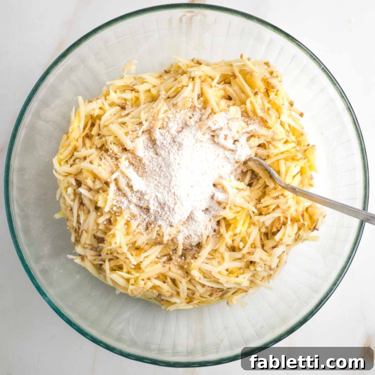 Grandma's Golden Potato Latkes 8 A bowl of shredded potatoes mixed with egg and onion, with matzo meal sprinkled on top, ready for the final mix.