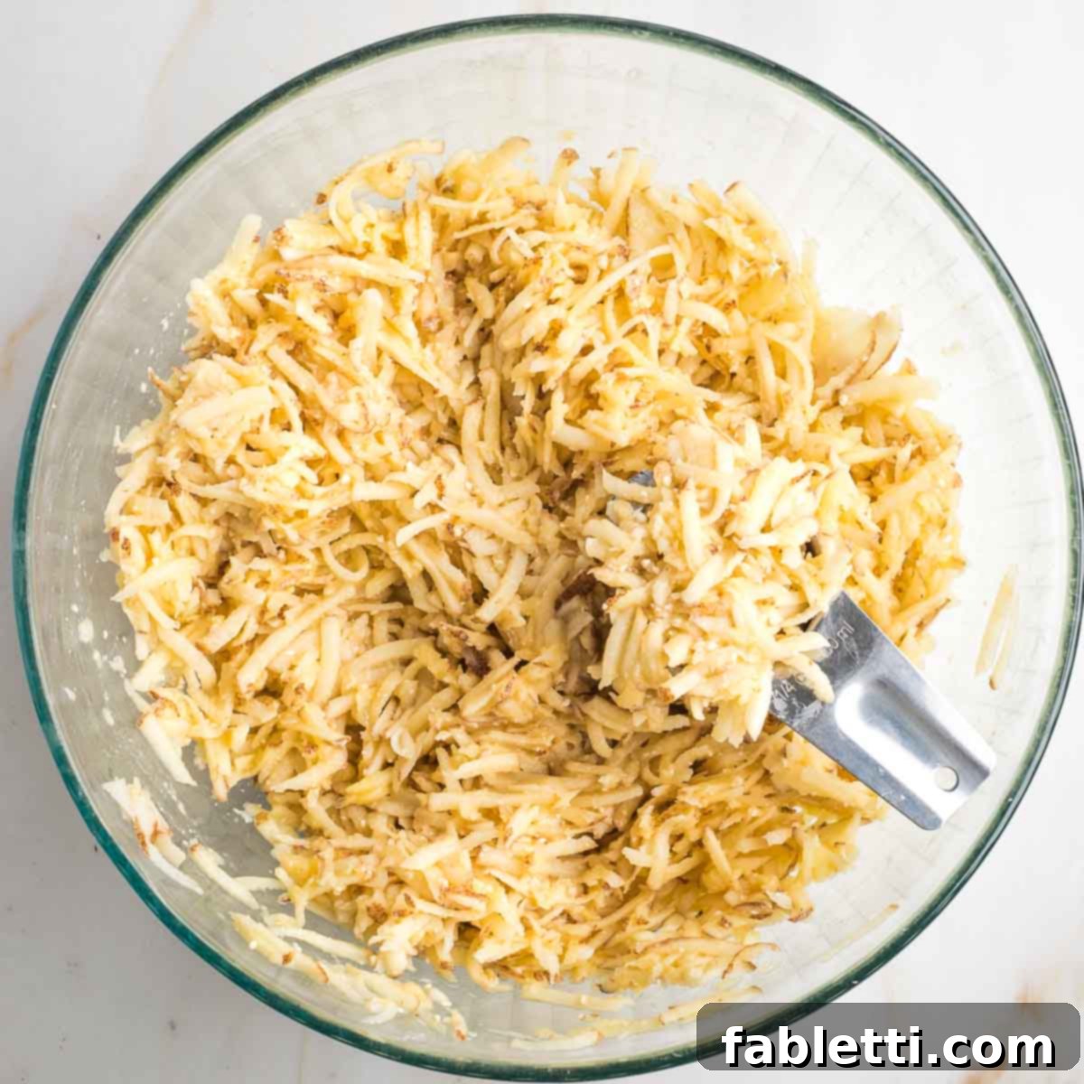 Grandma's Golden Potato Latkes 9 A ¼ cup measuring scoop lifting a portion of potato latke mixture from a large glass bowl, illustrating portioning.