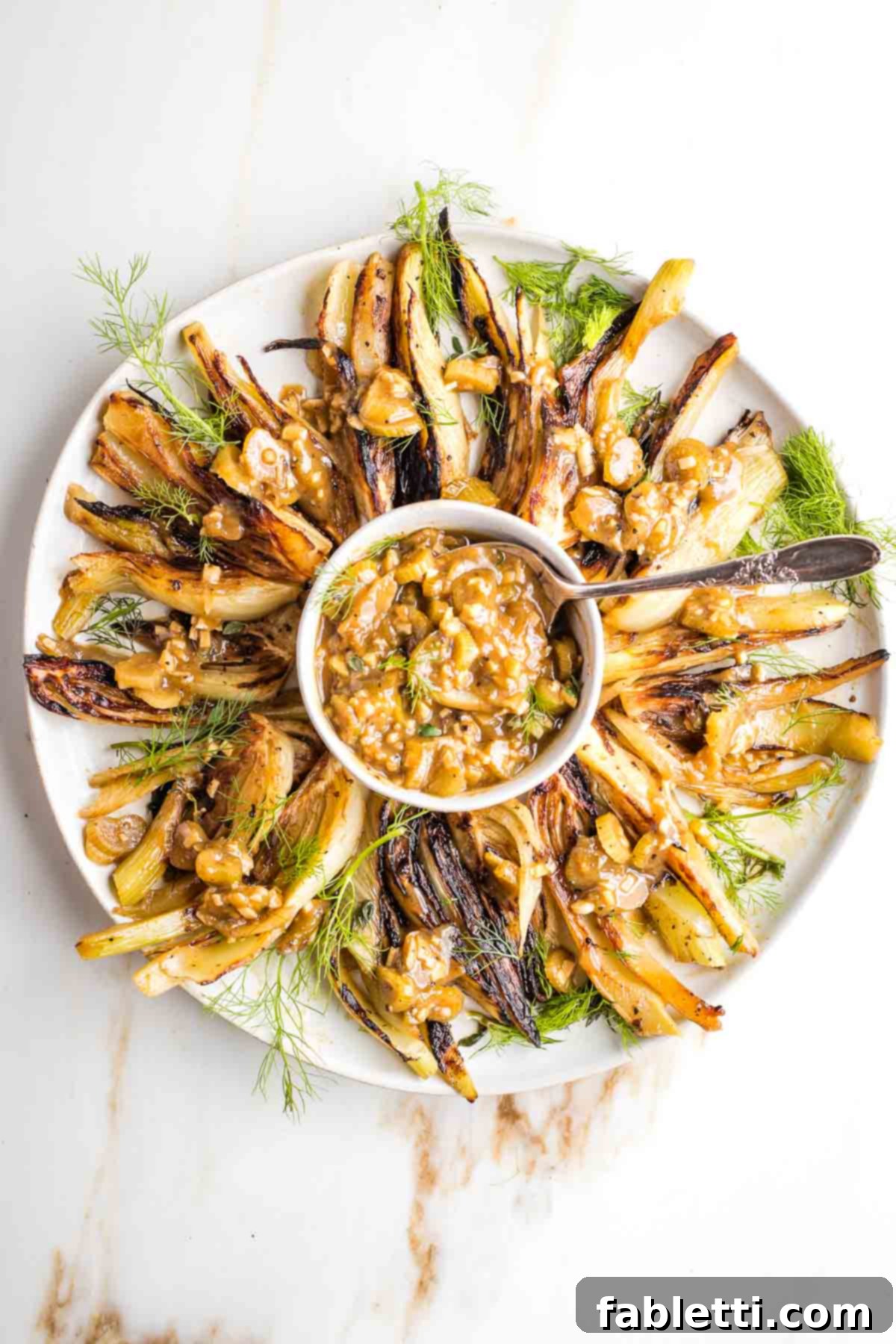 Wedges of browned and braised fennel elegantly arranged on a serving platter, showcasing their golden-brown edges and tender texture.