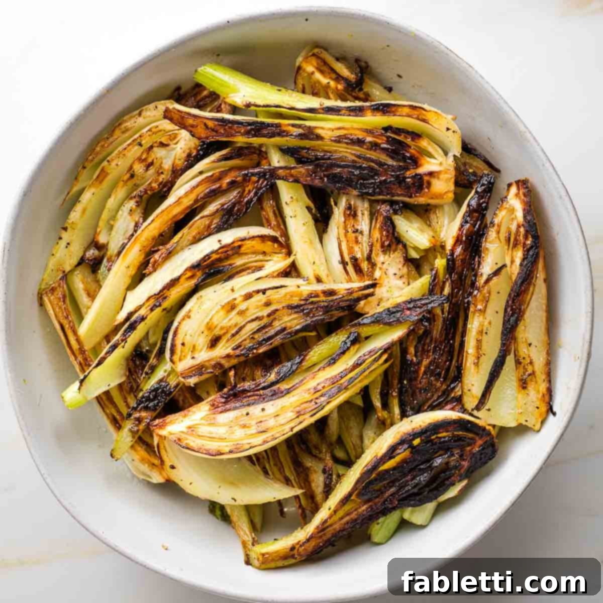 Golden brown fennel wedges, beautifully seared, resting in a pristine white bowl, awaiting the next stage of cooking.