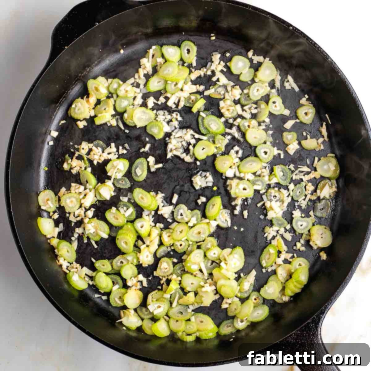 Finely sliced fennel stalks and minced garlic sizzling in a cast iron skillet, releasing their aromatic fragrances.