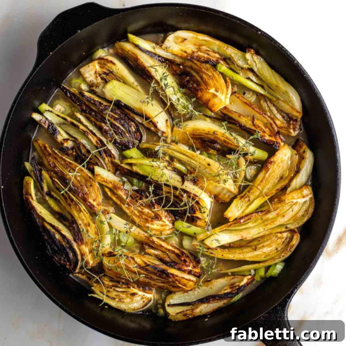 Golden wedges of seared fennel nestled back into the cast iron skillet, partially submerged in the braising liquid and topped with fresh thyme sprigs.