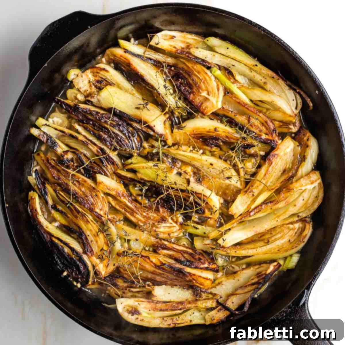 Braised and caramelized fennel wedges simmering gently in a cast iron skillet, covered and cooking to tender perfection.