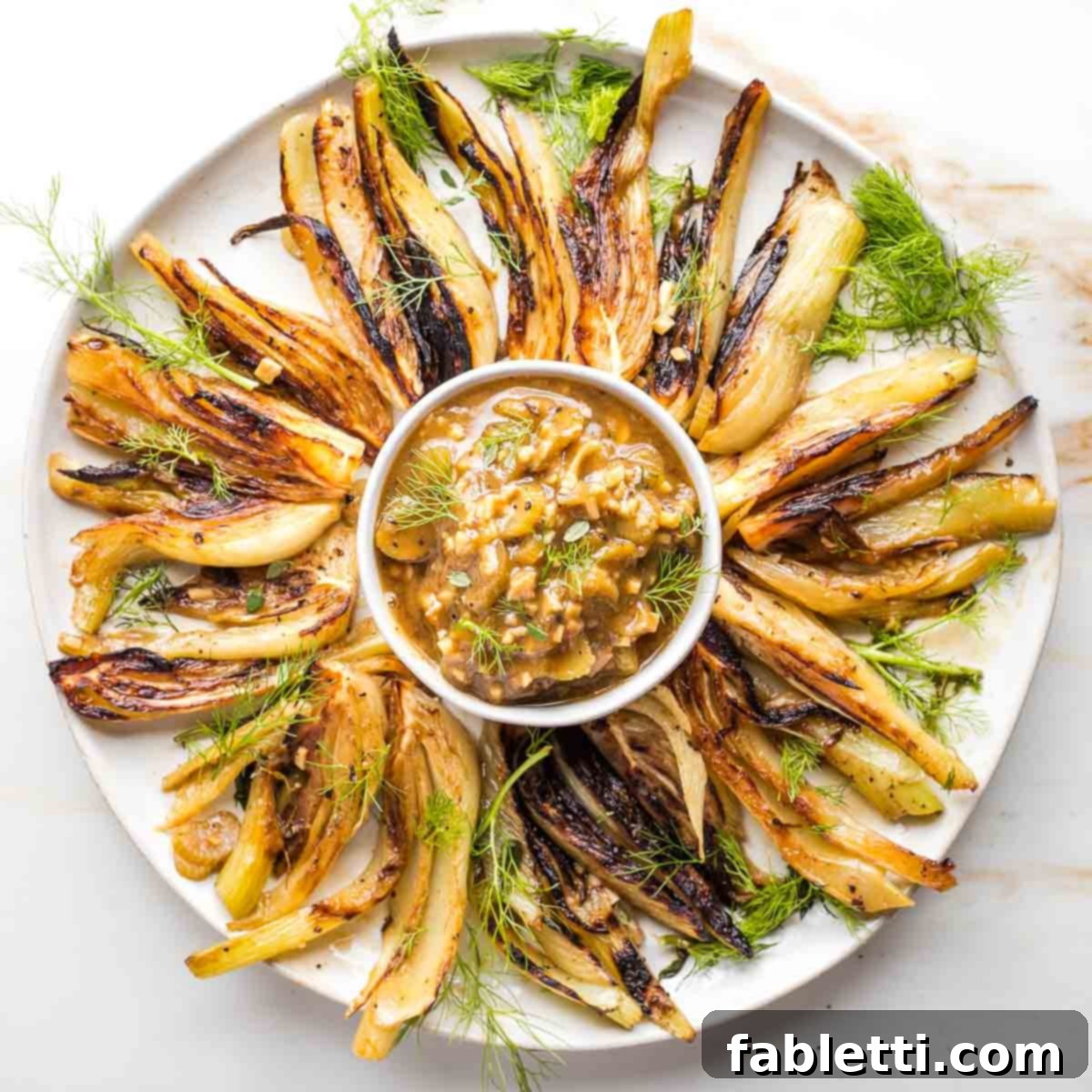 Browned fennel wedges beautifully arranged on a platter, with a bowl of chunky braising sauce in the center, ready to be served.