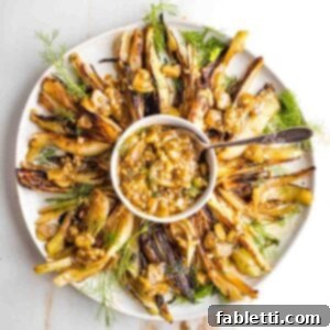 Braised fennel wedges arranged on a plate with a dollop of rich sauce in the center, garnished with fresh herbs.