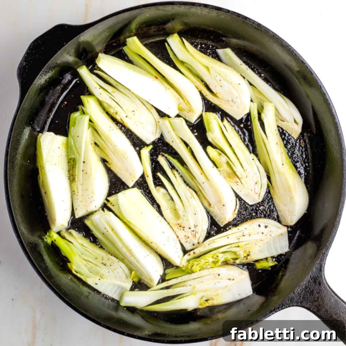 Fennel wedges generously seasoned with salt and pepper, arranged in a single layer in a hot cast iron skillet, ready for searing.