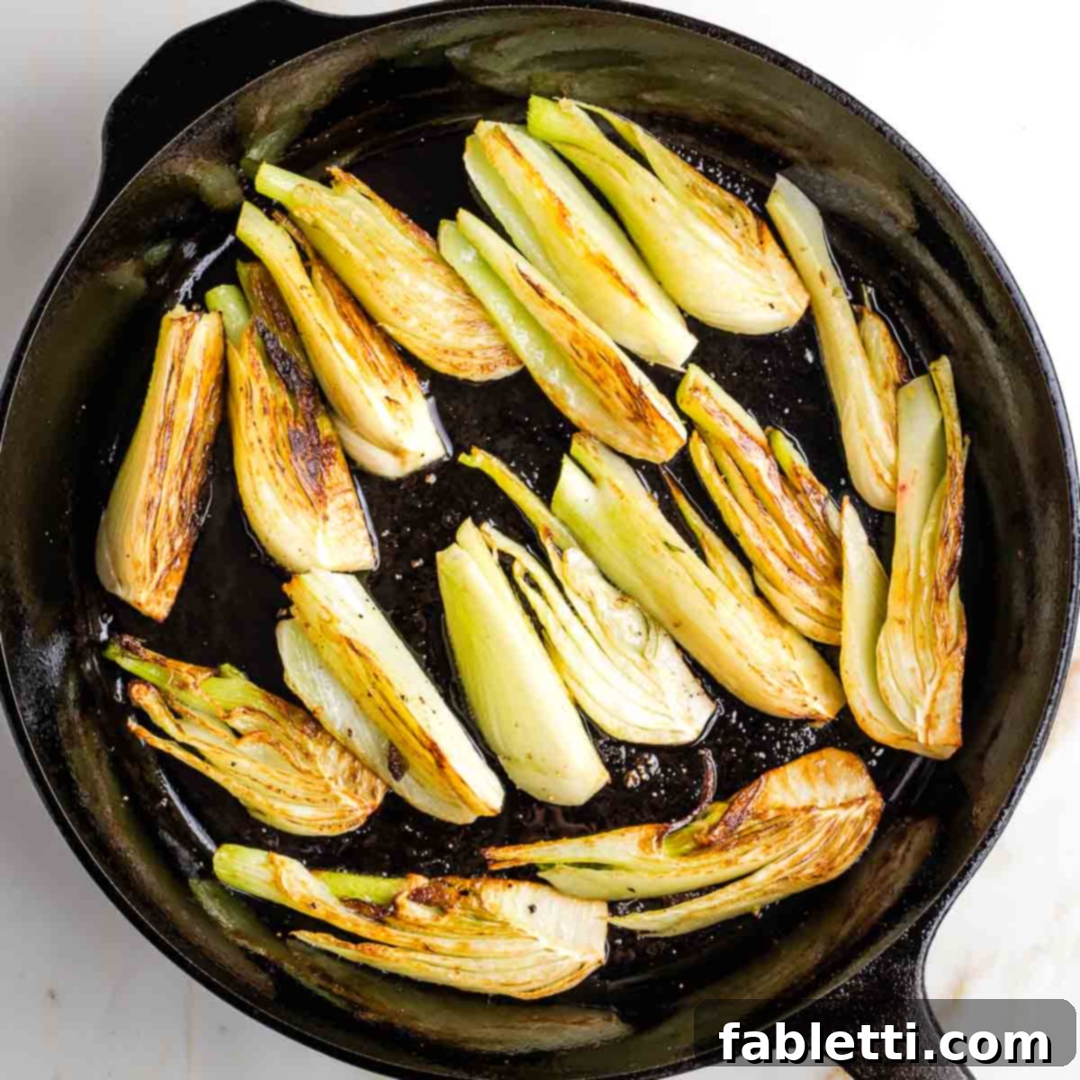Beautifully browned fennel wedges, caramelized and golden, resting in a cast iron skillet after searing.