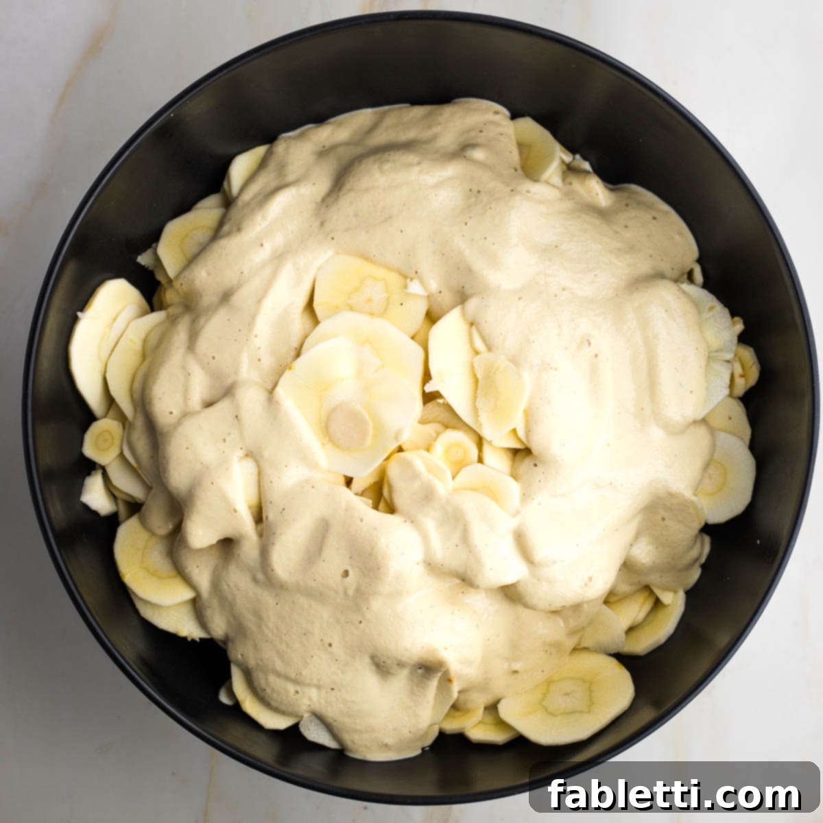 Luscious Vegan Parsnip Gratin 15 Black bowl with thin slices of parsnips, covered in cream sauce.