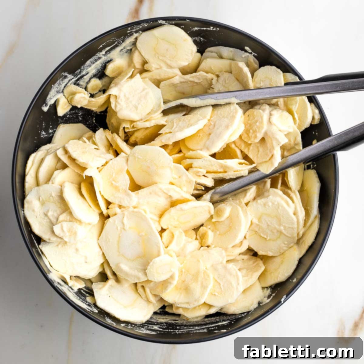 Luscious Vegan Parsnip Gratin 16 Tongs tossing sliced parsnips with cream sauce.